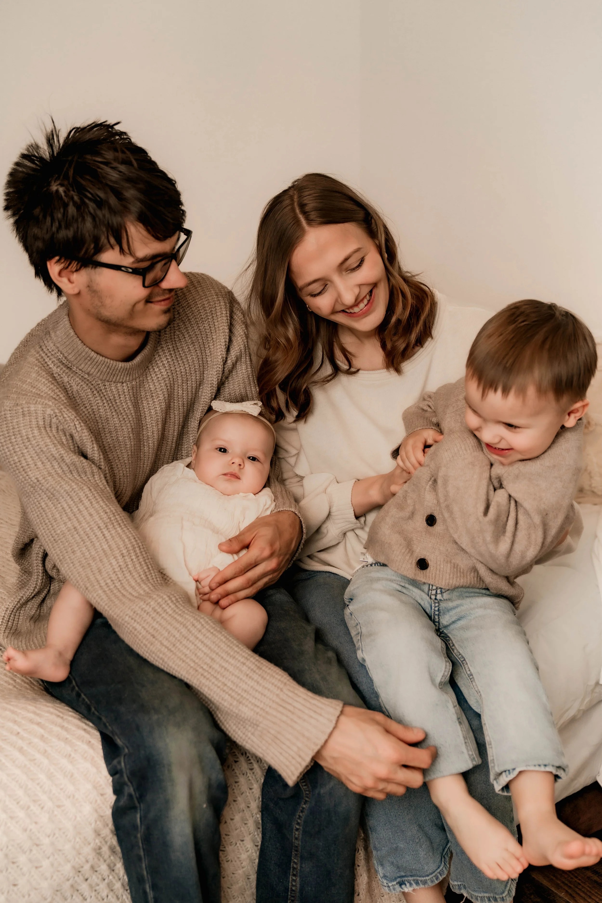 A family of four sitting on a couch, smiling and playing with each other in a cozy living room.