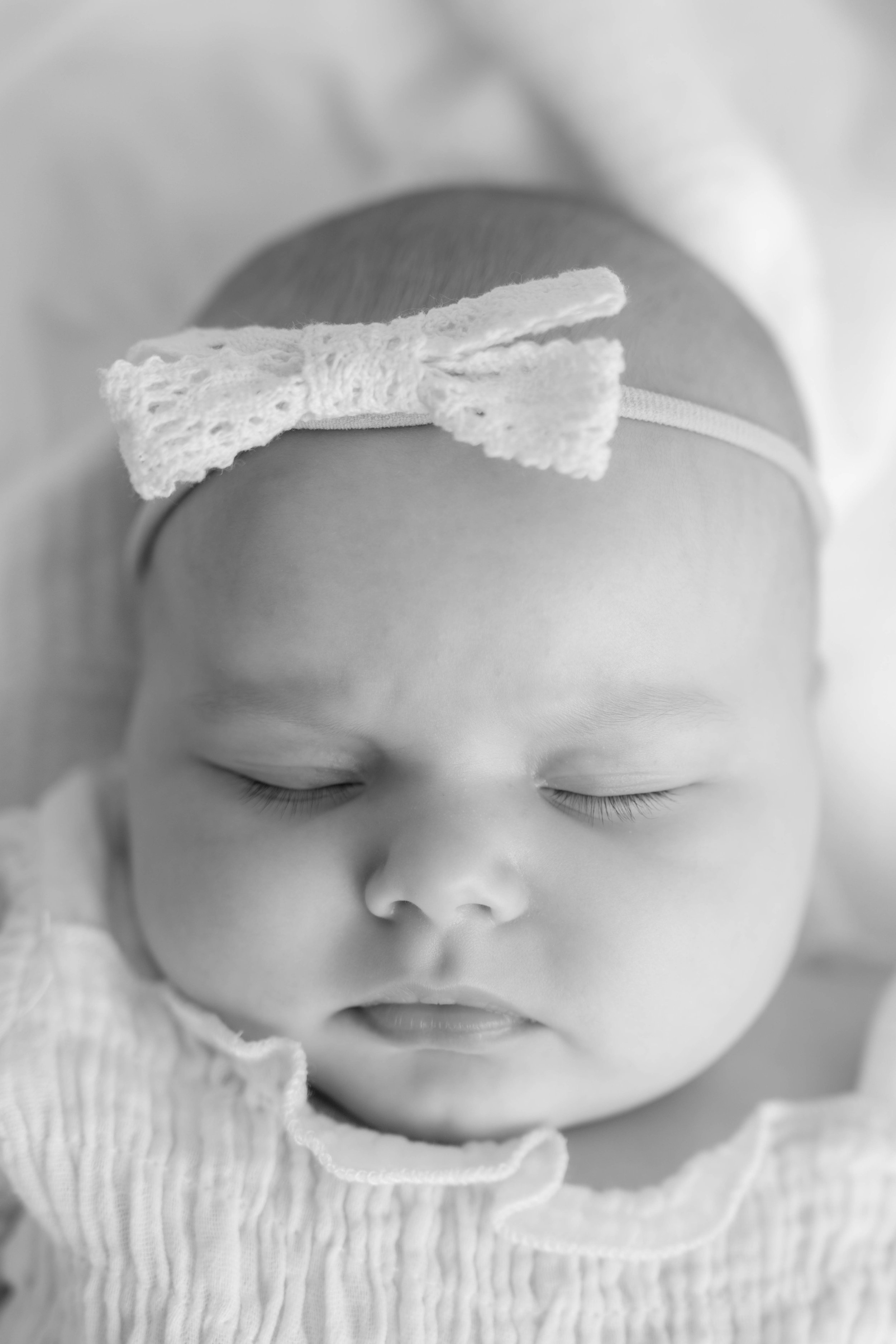 Black and white close-up of a sleeping baby wearing a headband with a bow.