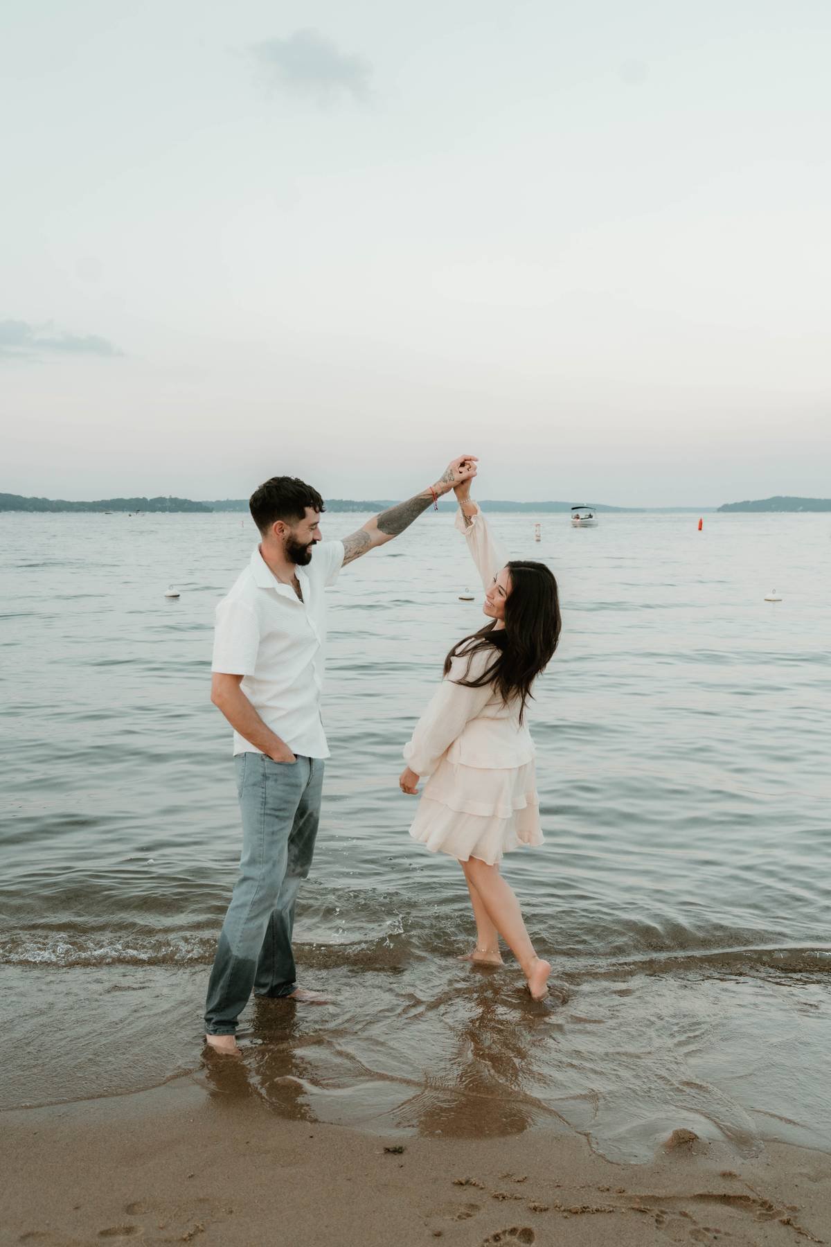 A man and woman dancing on the beach by the water, with boats and buoys in the background