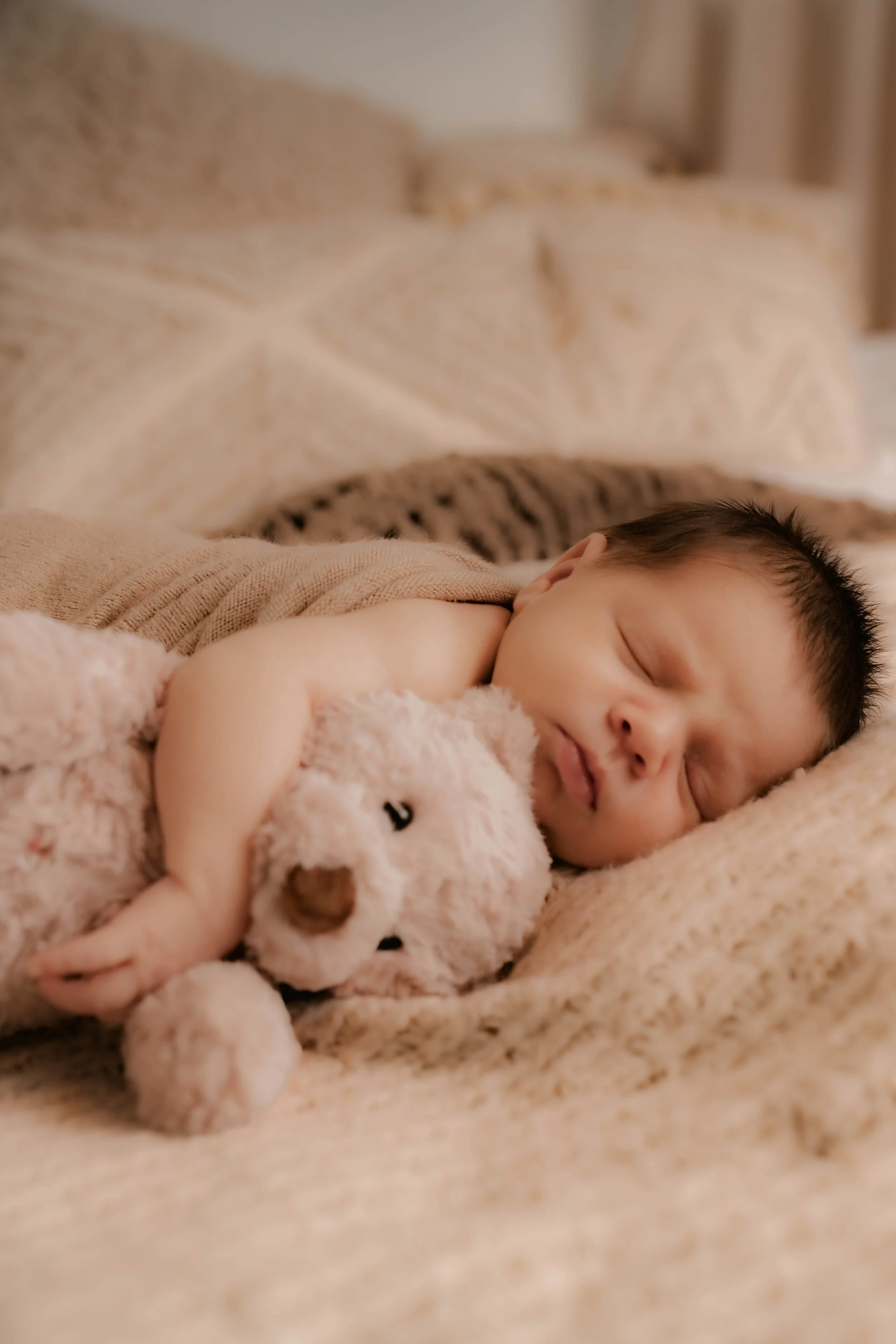 A sleeping baby holding a plush bear stuffed animal on a cozy bed.