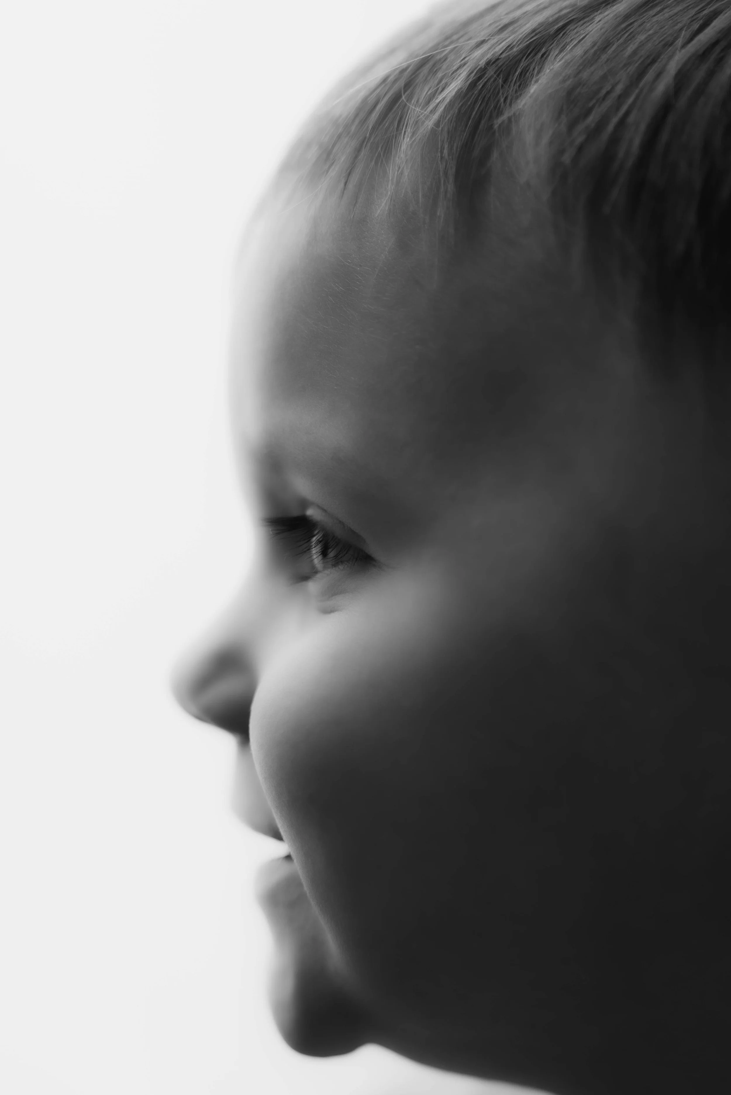 Close-up black and white portrait of a young child's face in profile view, with soft lighting highlighting facial features.