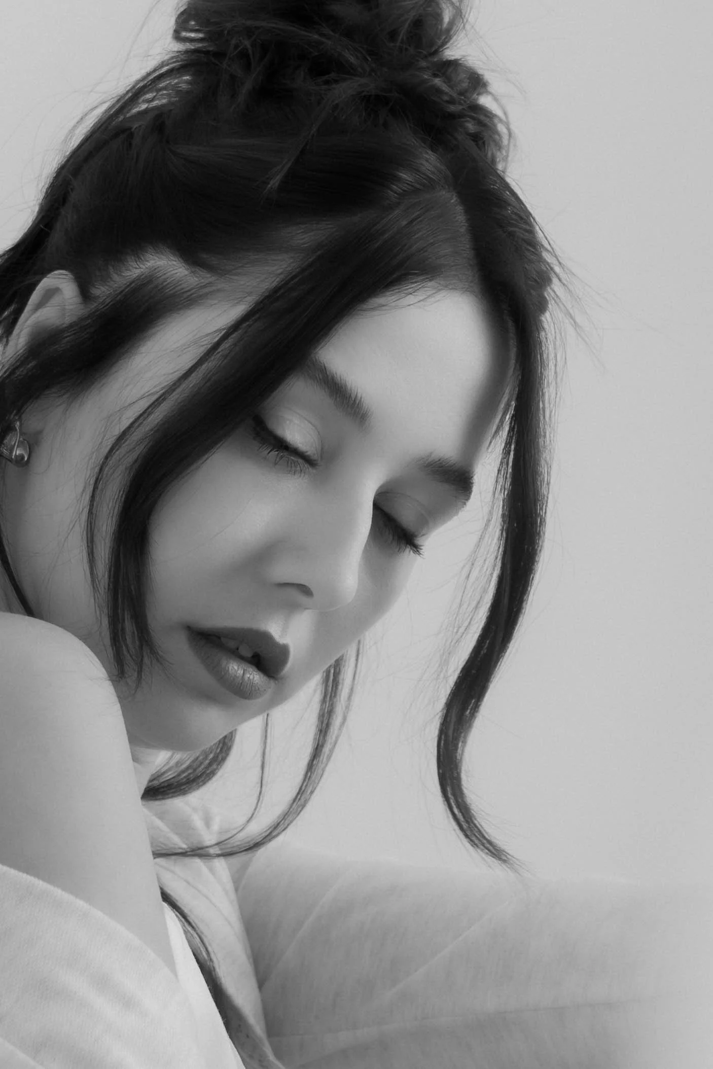 A black and white close-up photo of a woman with eyes closed, dark hair in loose waves, and slightly parted lips.