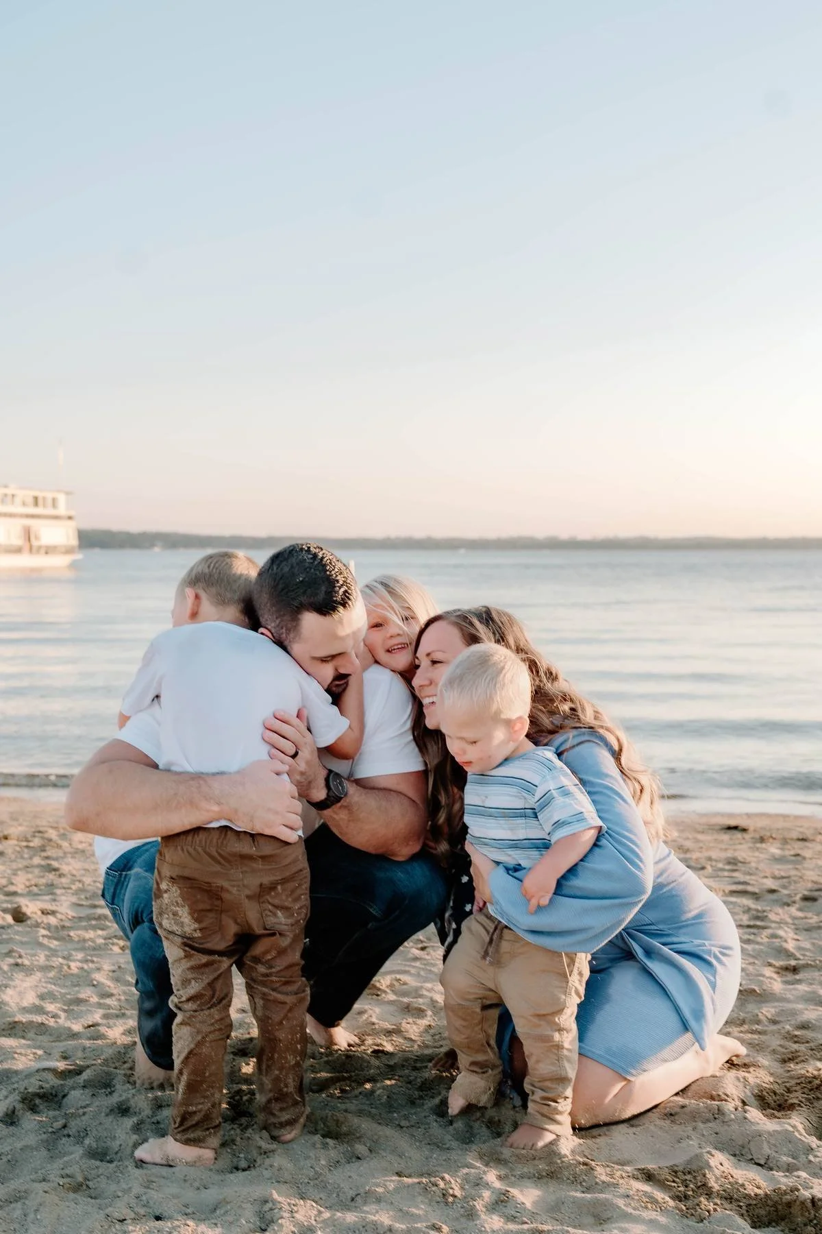 Family on the beach hugging by the water at sunset.