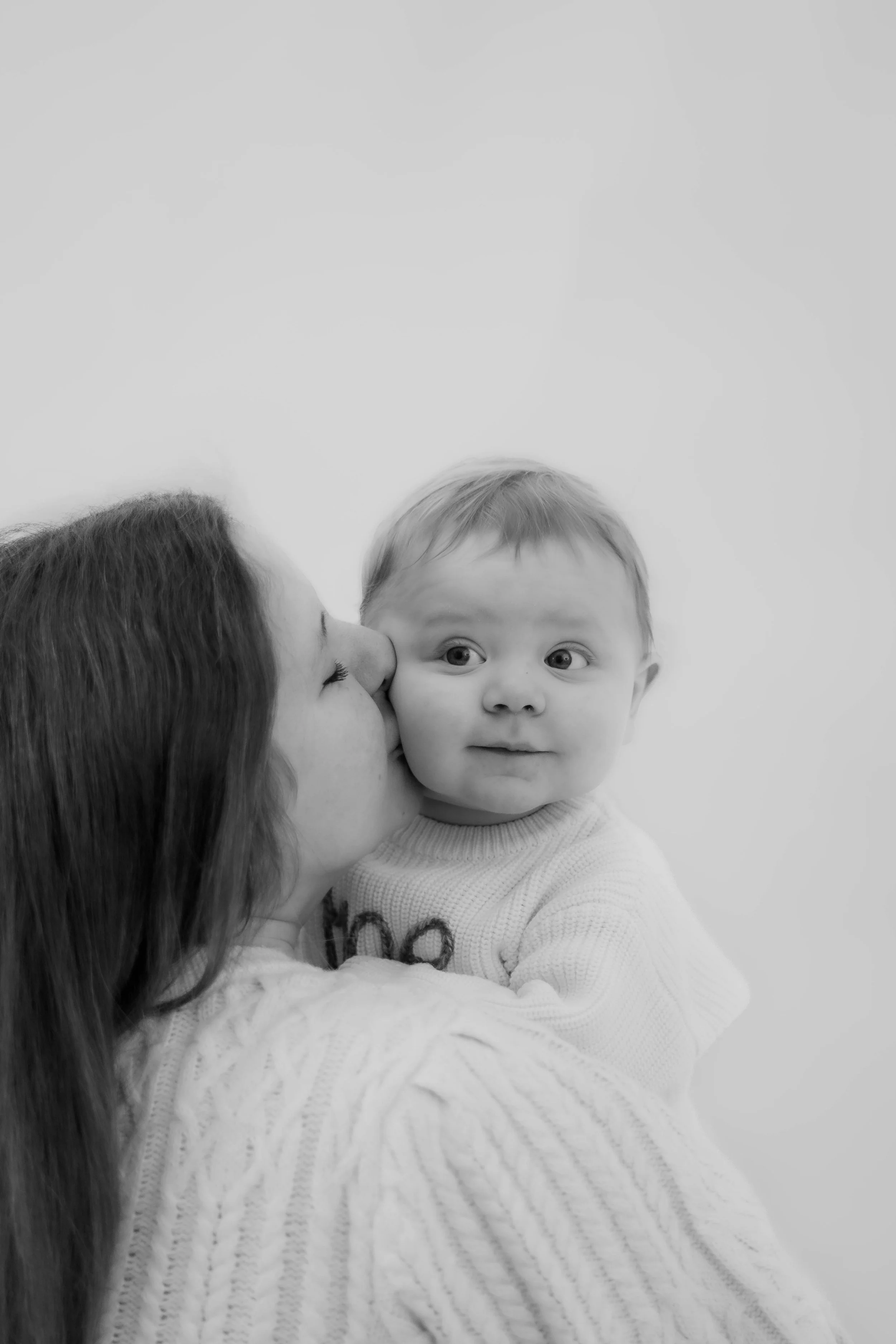 Woman kissing a young boy on the cheek, the boy has a surprised look, black and white photo