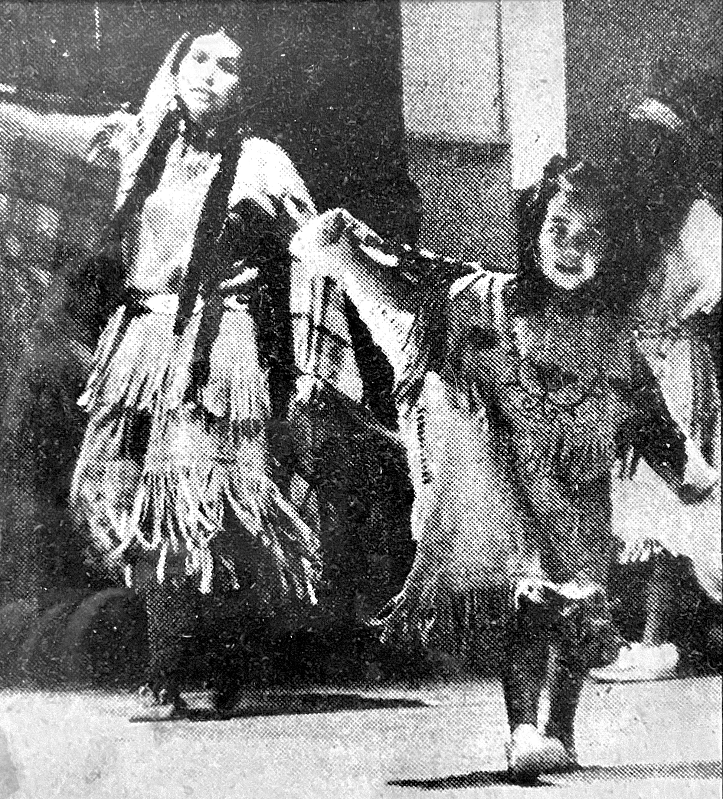 Two women dressed in traditional Native American clothing, dancing or performing in a cultural setting.