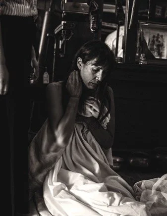 A woman sitting on the ground with her hand on her neck, looking down, in black and white.