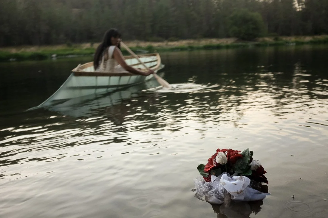 A woman in a boat on a lake, near a floral bouquet floating on the water.