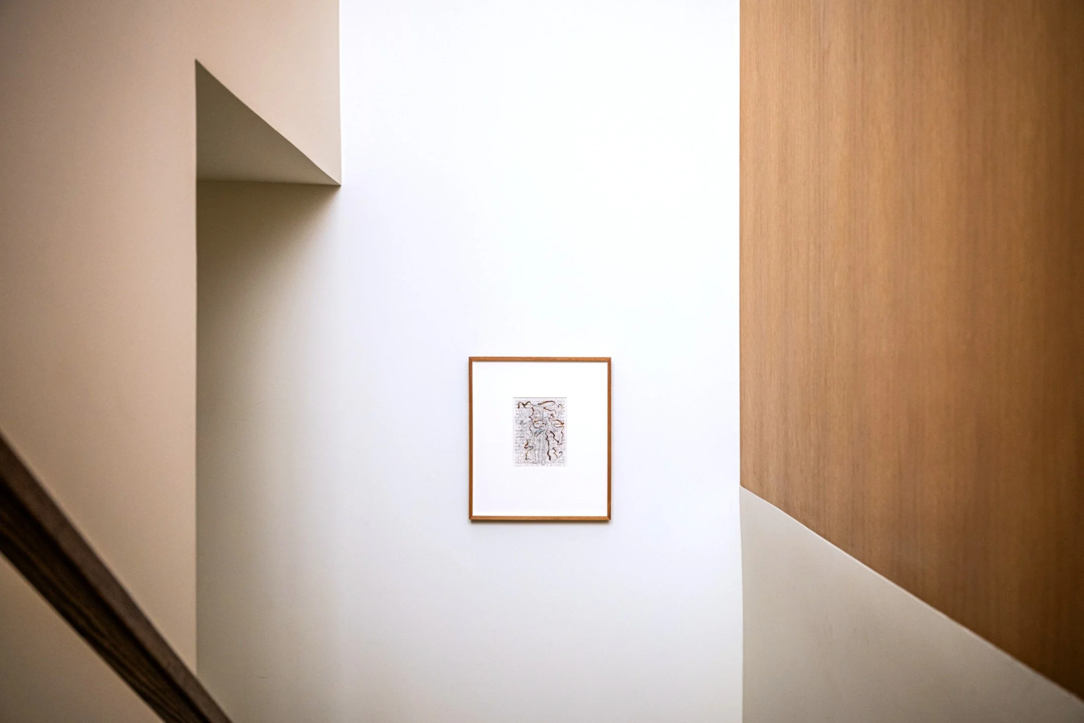 Architectural stair hall with clean white walls, warm wood paneling, and framed artwork, emphasizing minimalist composition in modern interior design.