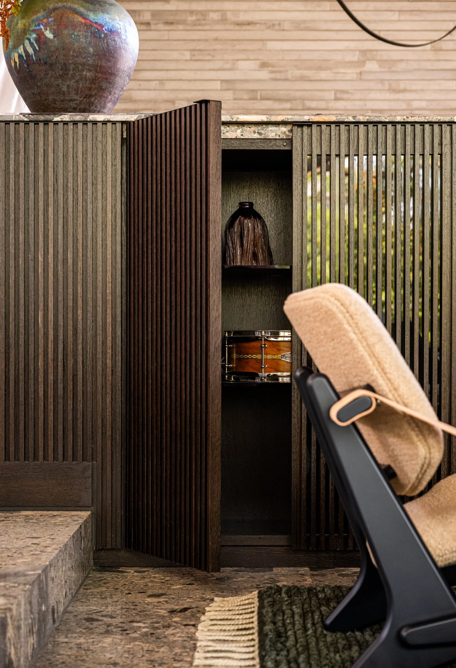Custom wood cabinet with slatted doors and integrated shelving, paired with warm materials and modern furniture in a luxury interior. Vintage Jumbo chairs Olof Ottelin, Finland in foreground.