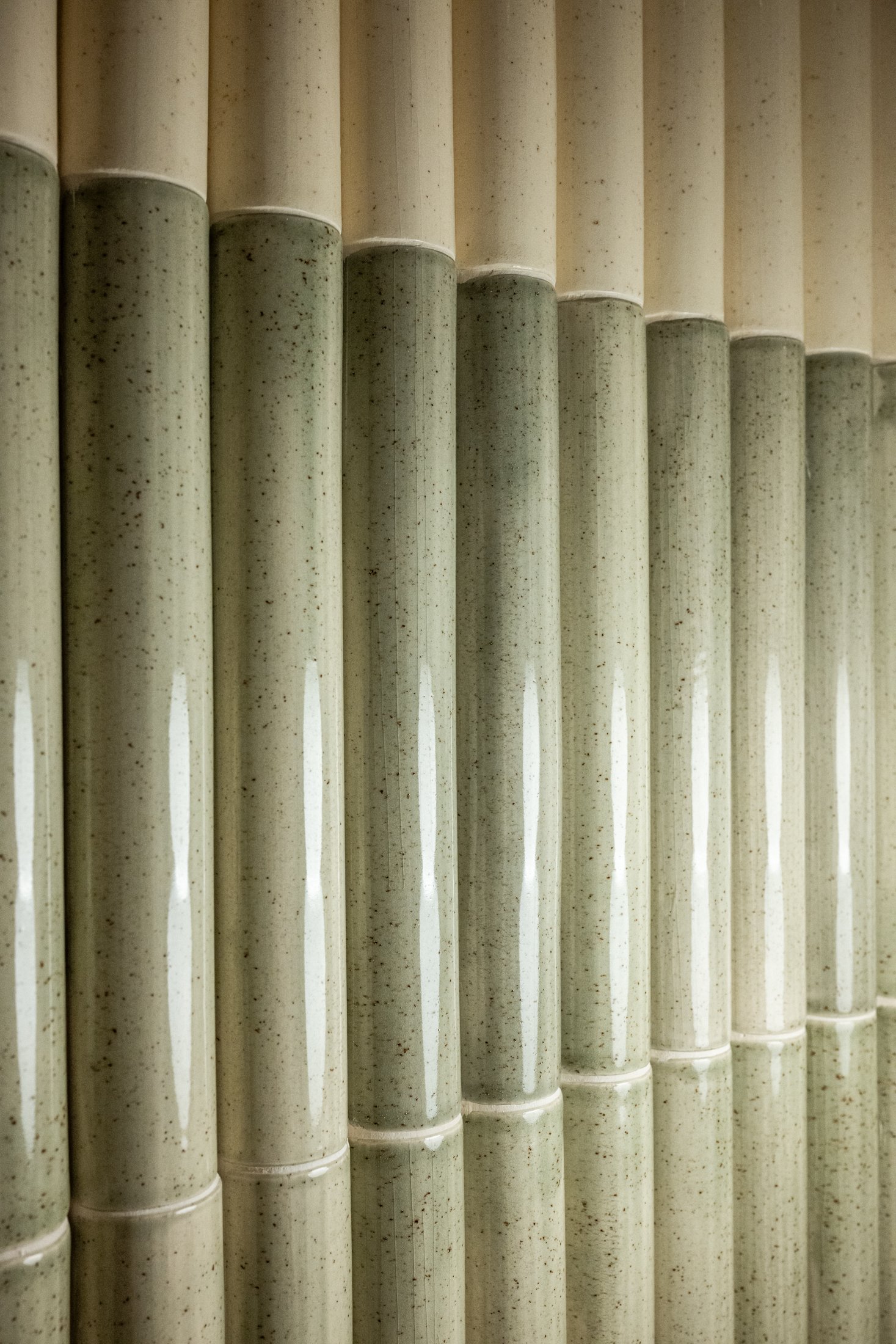 Vertical custom JRD ceramic tile detail with soft green glaze and subtle speckling, emphasizing texture and repetition in contemporary interior design.