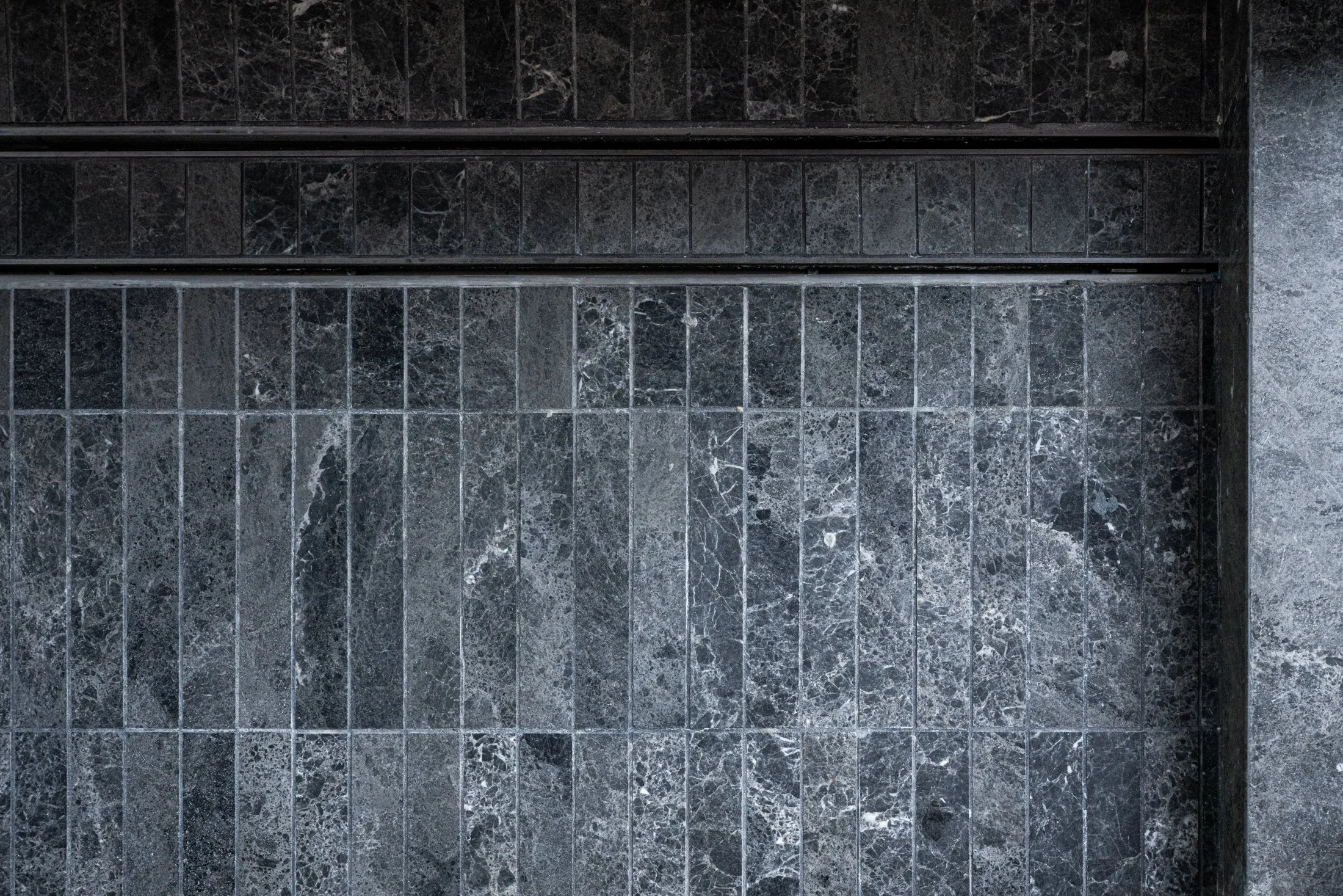 Dark stone tile shower floor detail with linear pattern, showcasing natural veining and refined material application in a contemporary bathroom.