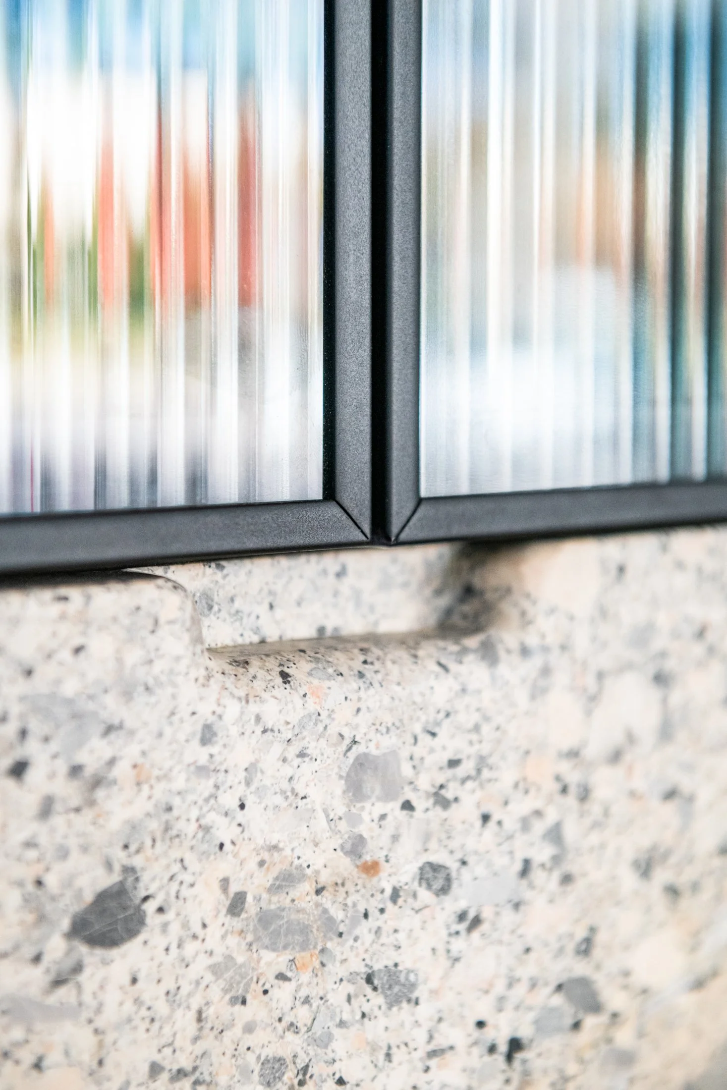 Detail of grey ceppo finger pull and ribbed glass cabinetry, highlighting edge conditions and refined junctions between materials.