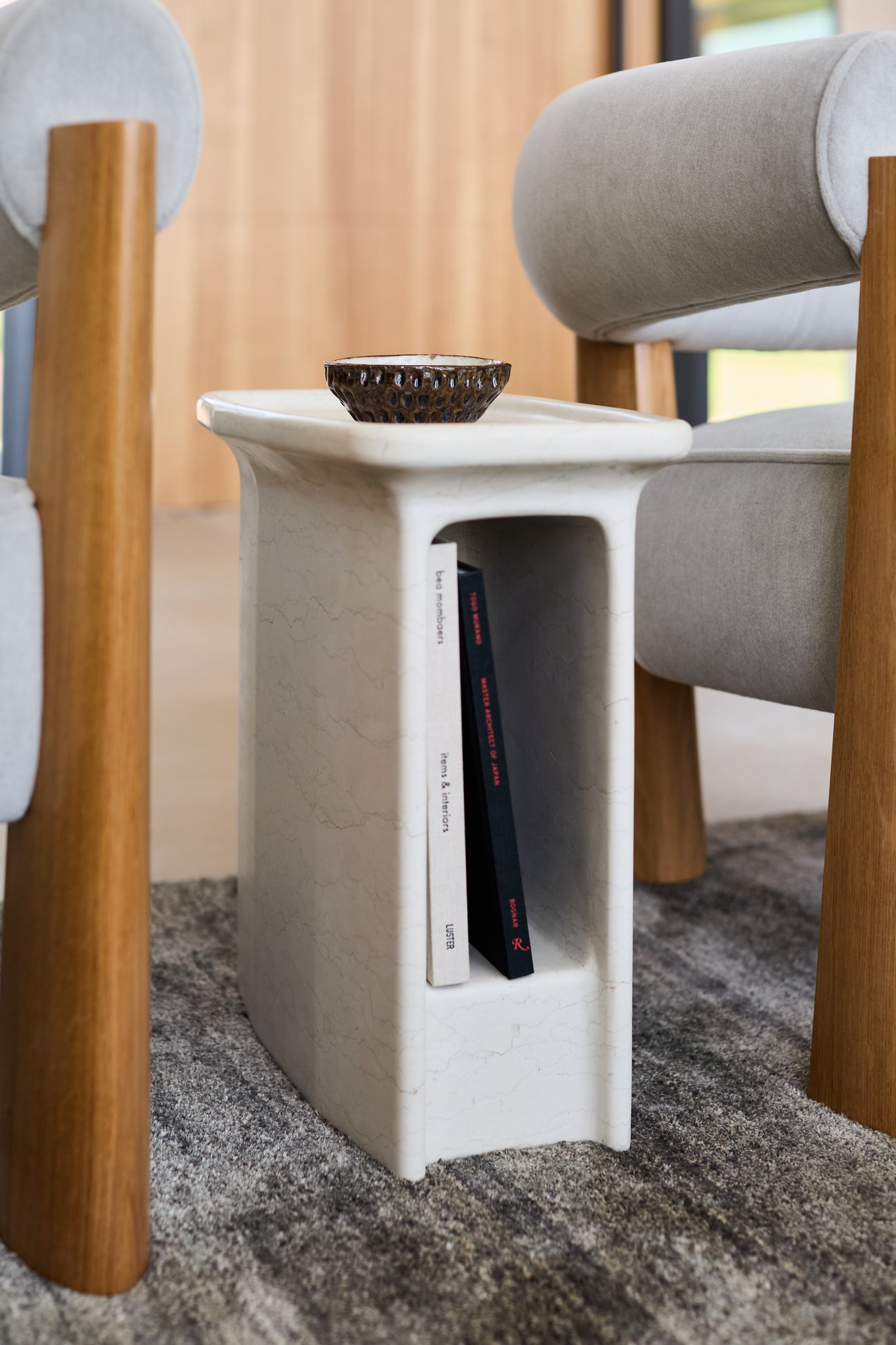 Modern marble side table with open storage niche between upholstered lounge chairs.  Rische collection Bishop drinks table in bianco perlino marble MAXIME BOUTILLIER chairs