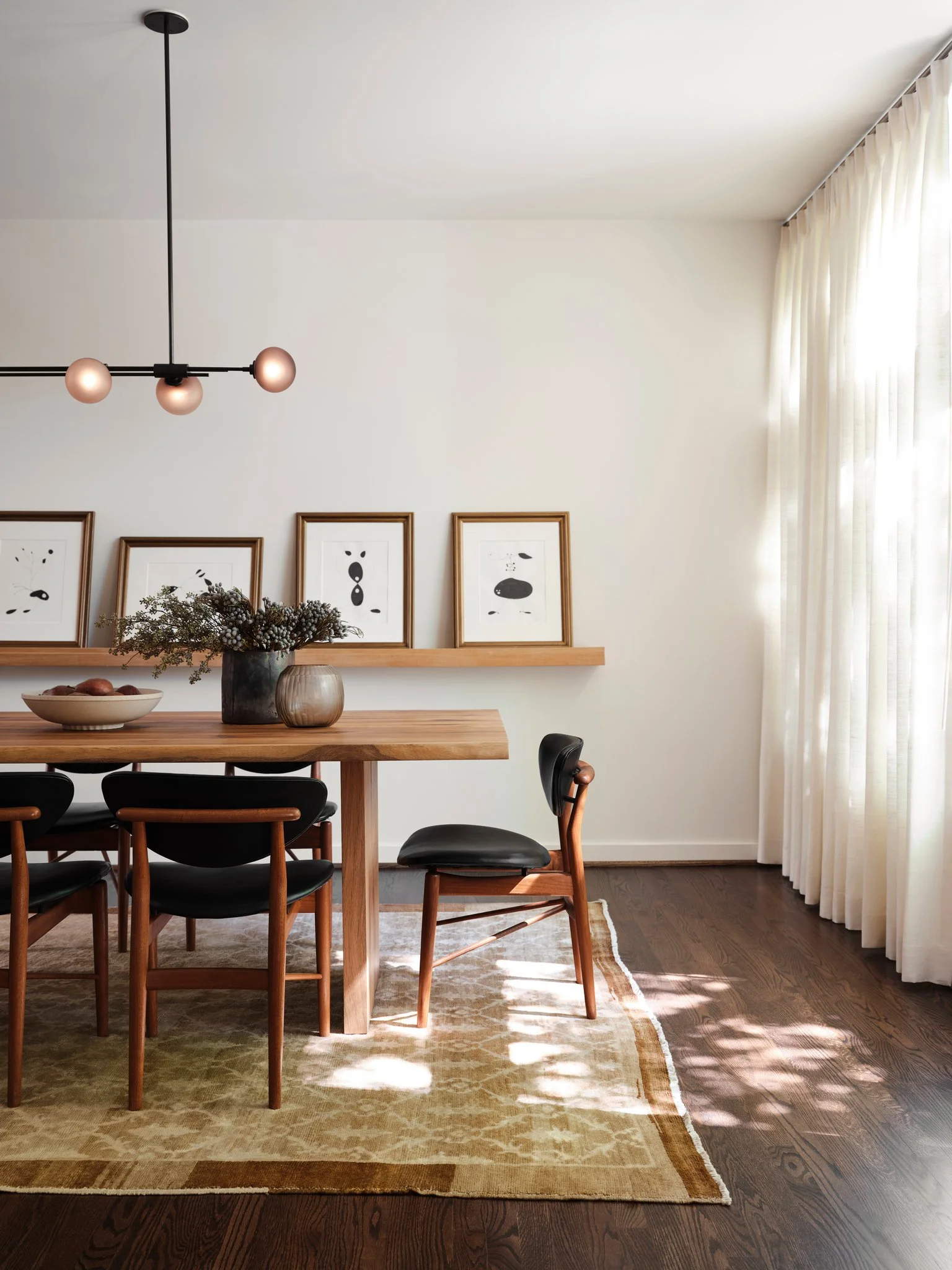 Contemporary dining room with wood table, black leather vintage chairs by Finn Juhl , and minimalist Articolo lighting, framed by soft drapery and natural light.