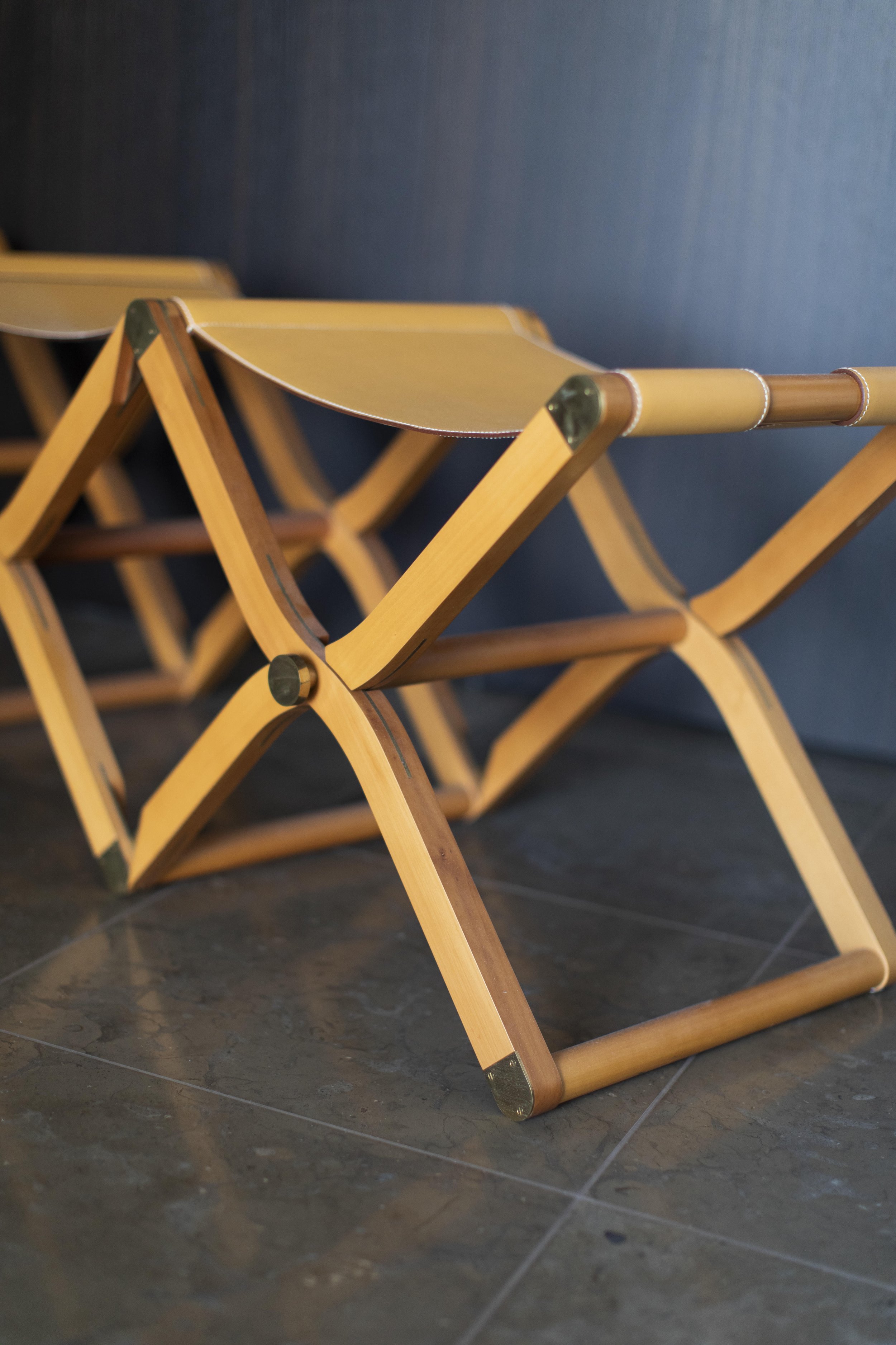 Modern leather folding benches beneath contemporary artwork installation on dark wood architectural wall hermes pippa collection Rena Dumas and Peter Coles