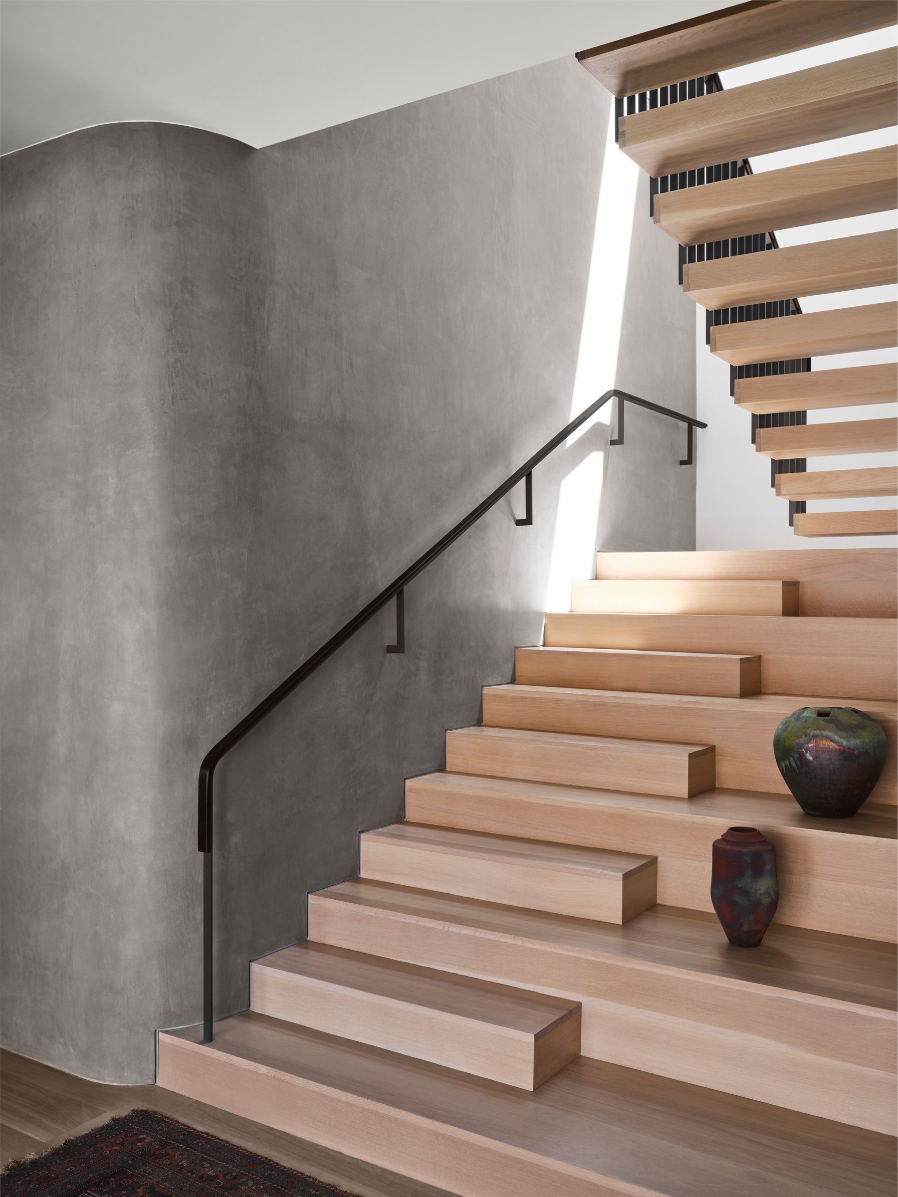 Open wood stair with floating treads and plaster surround, emphasizing light, proportion, and restrained material contrast.