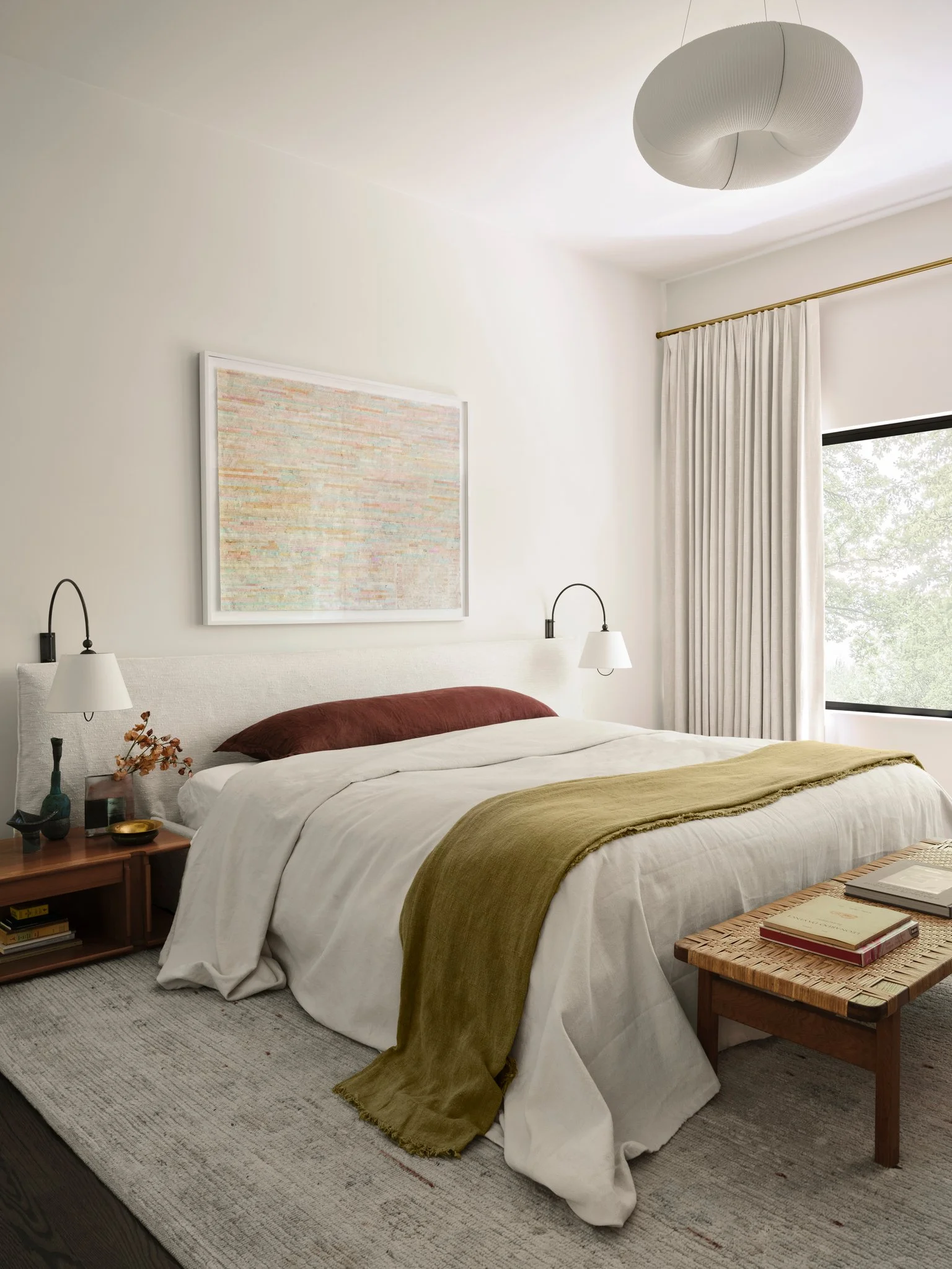 Modern bedroom with upholstered headboard, layered textiles, and sculptural lighting, designed with a calm, material-driven aesthetic. Vintage bedside tables by Bernini and a woven cane bench by Bruno Mattheson.  Lamps by Kalmar. 