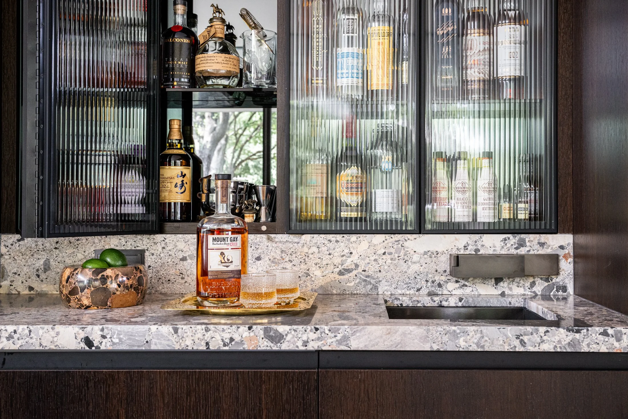 Backlit bar with ribbed glass cabinetry and terrazzo countertop, layering transparency, texture, and reflective materials.
