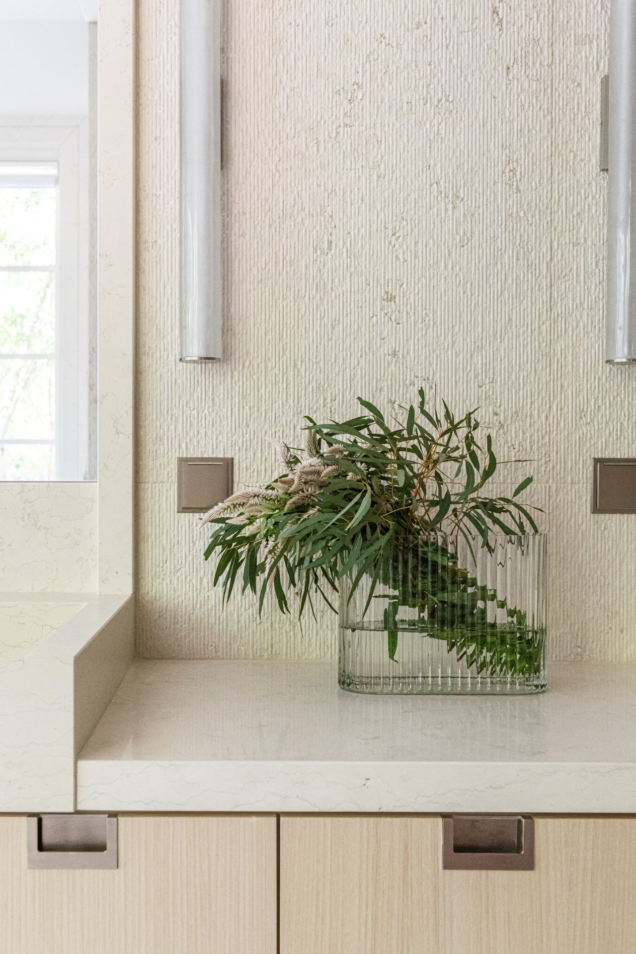 Textured bianco perlino wall detail with integrated stone countertop, floral arrangement, and refined bath millwork in a luxury residence.