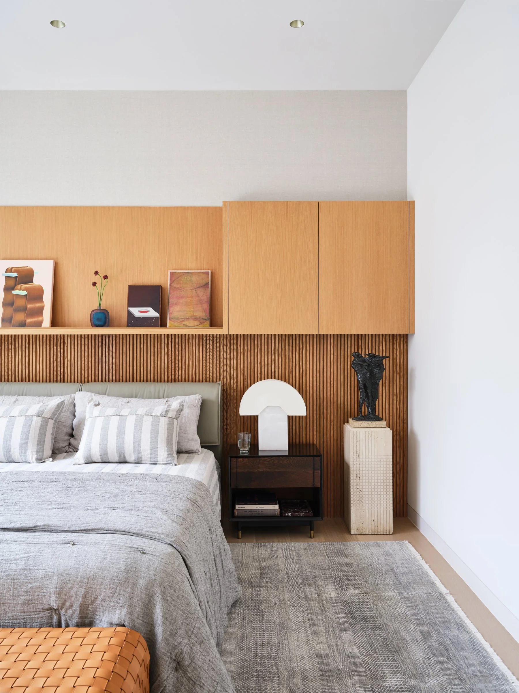 Bedroom detail with fluted wood paneling, integrated cabinetry, and sculptural lighting, creating a restrained and composed interior.