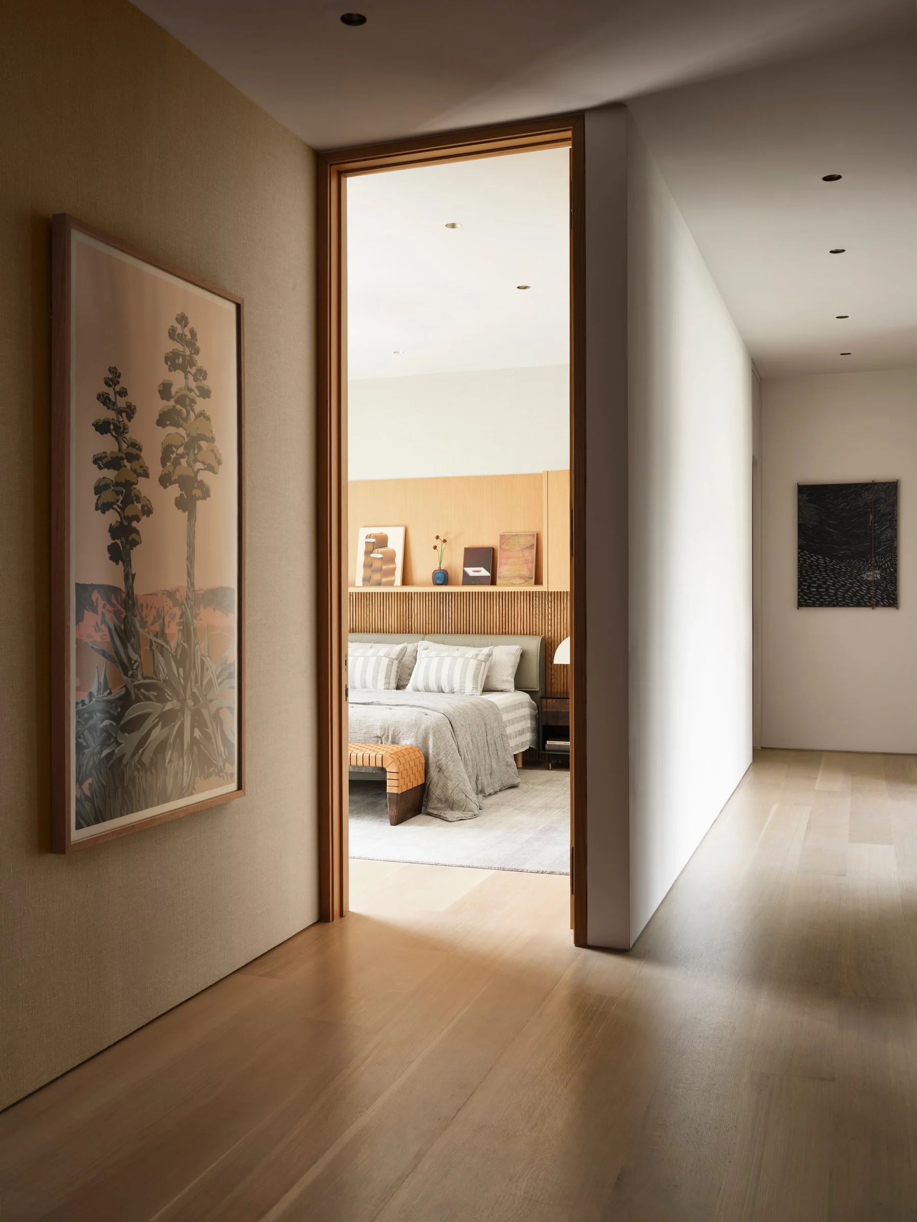 Framed view into bedroom with custom wood headboard wall and integrated storage, emphasizing proportion and quiet material layering.