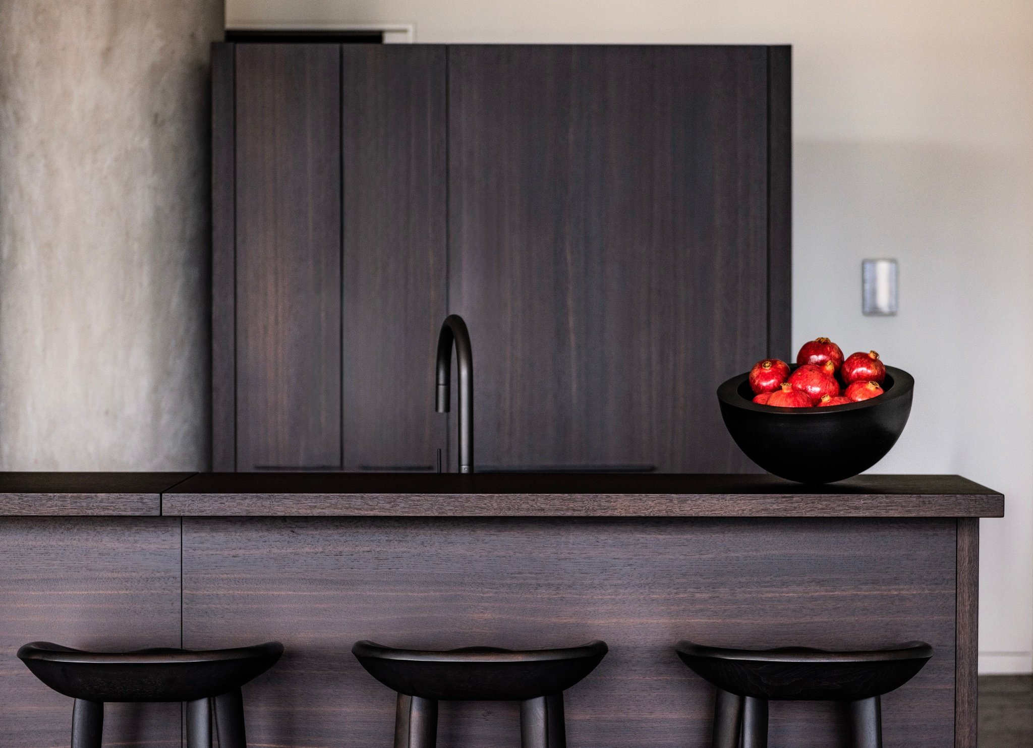 Modern luxury kitchen with dark wood cabinetry, minimalist island, black bar stools, and sculptural bowl centerpiece john pawson, when objects work, bassam fellows, poliform