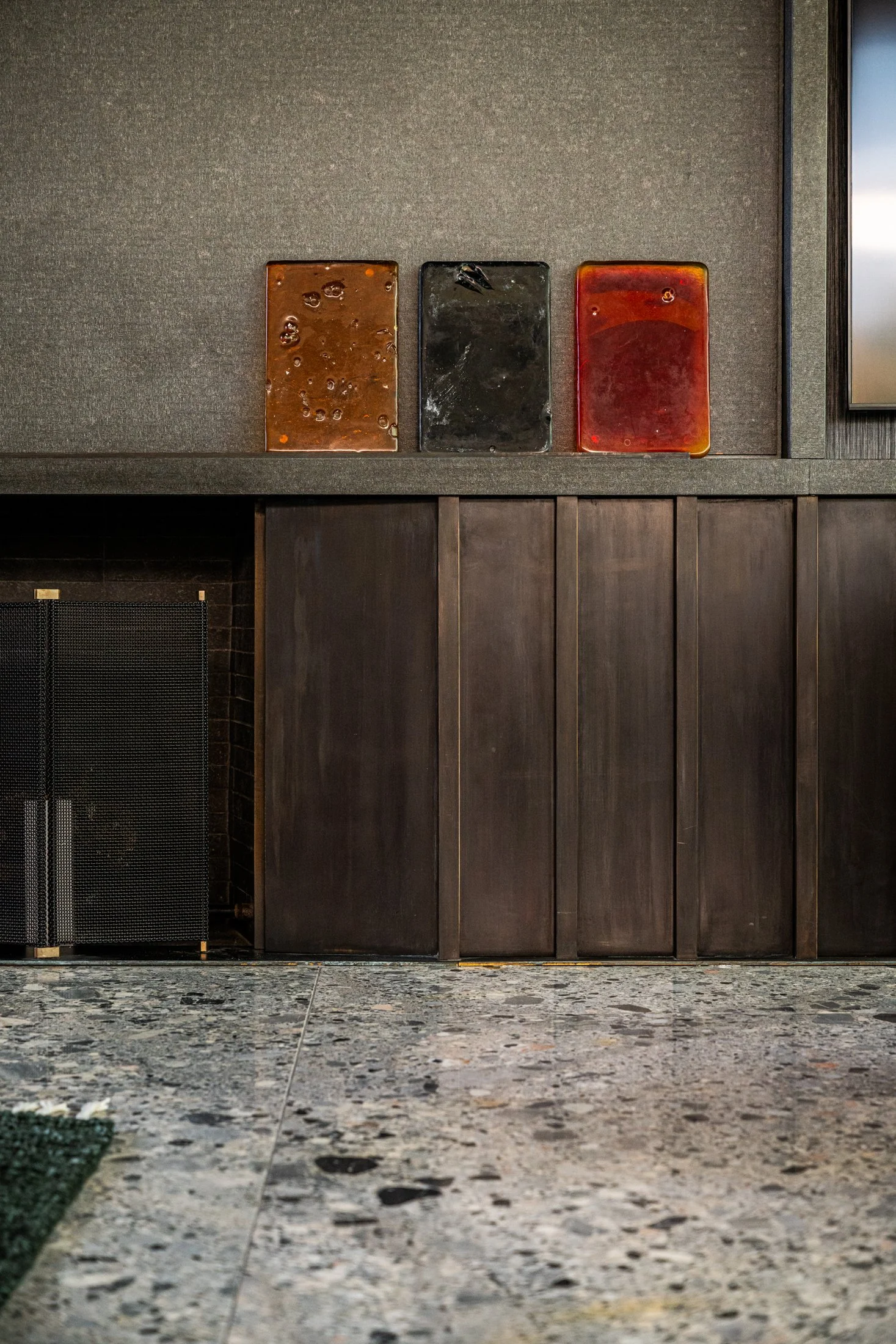 Custom fireplace surround with Blackened Brass paneling and stone flooring, featuring sculptural glass objects in a contemporary living space.