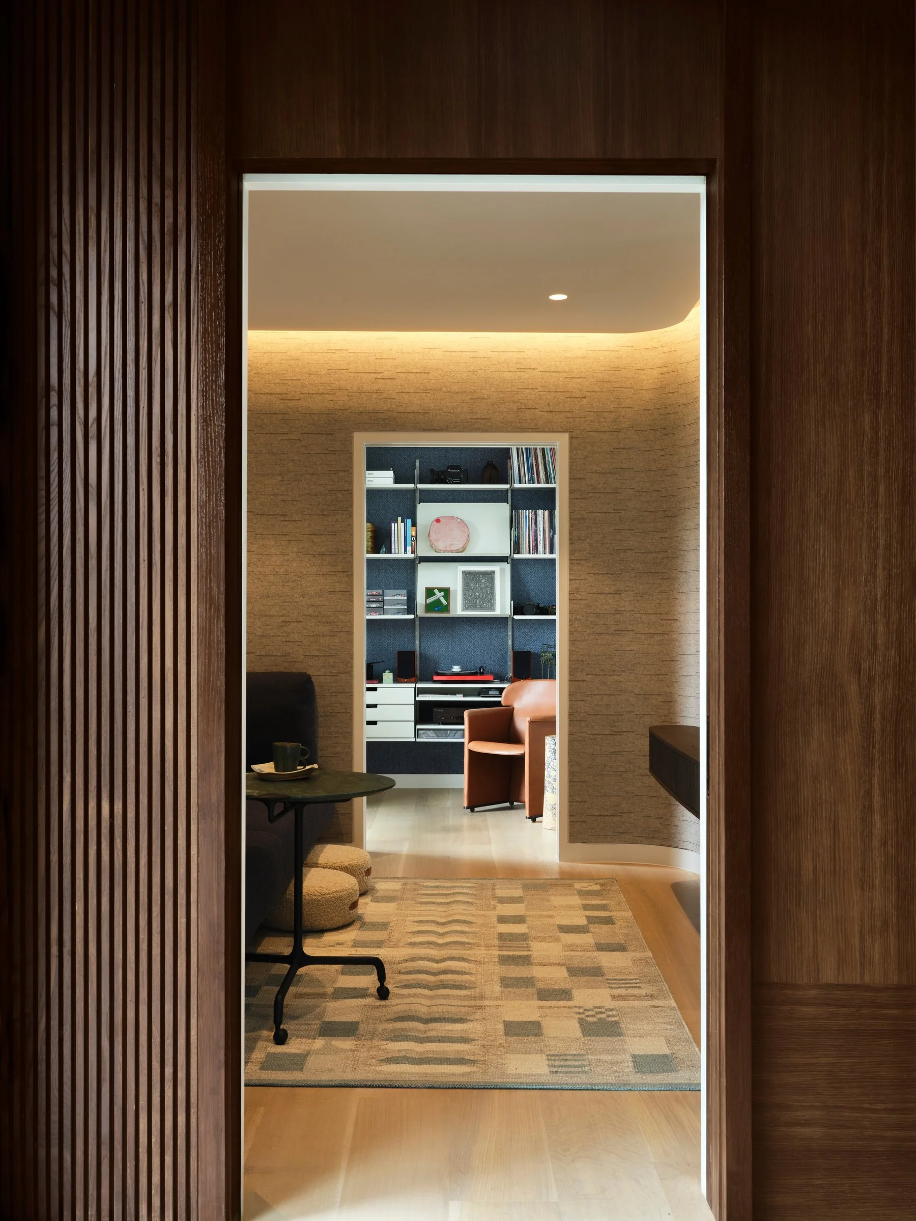 Framed view through wood-paneled opening into a curated sitting room with built-in shelving and layered textiles.