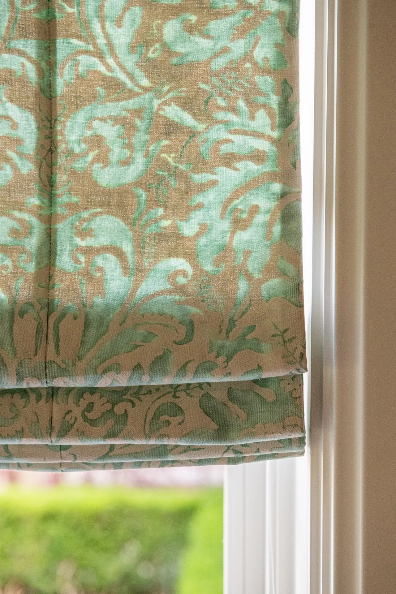 A tailored Roman shade in hand-printed silk Fortuny textile introduces subtle pattern and softness to the architecture. Muted green and warm neutral tones add quiet richness without disrupting restraint.