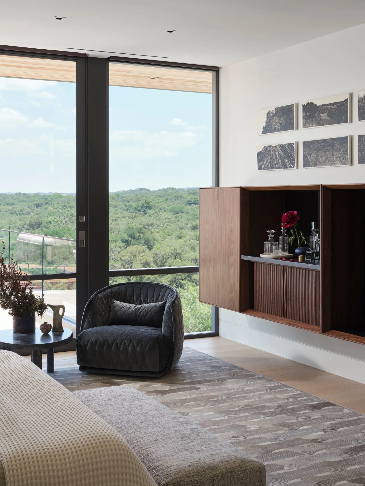 Quiet seating area beside expansive glass overlooking wooded landscape. Upholstered lounge chair, sculptural cabinet, and curated objects create a refined moment within the home.  Moroso chairs, cabinet by jader almeida.