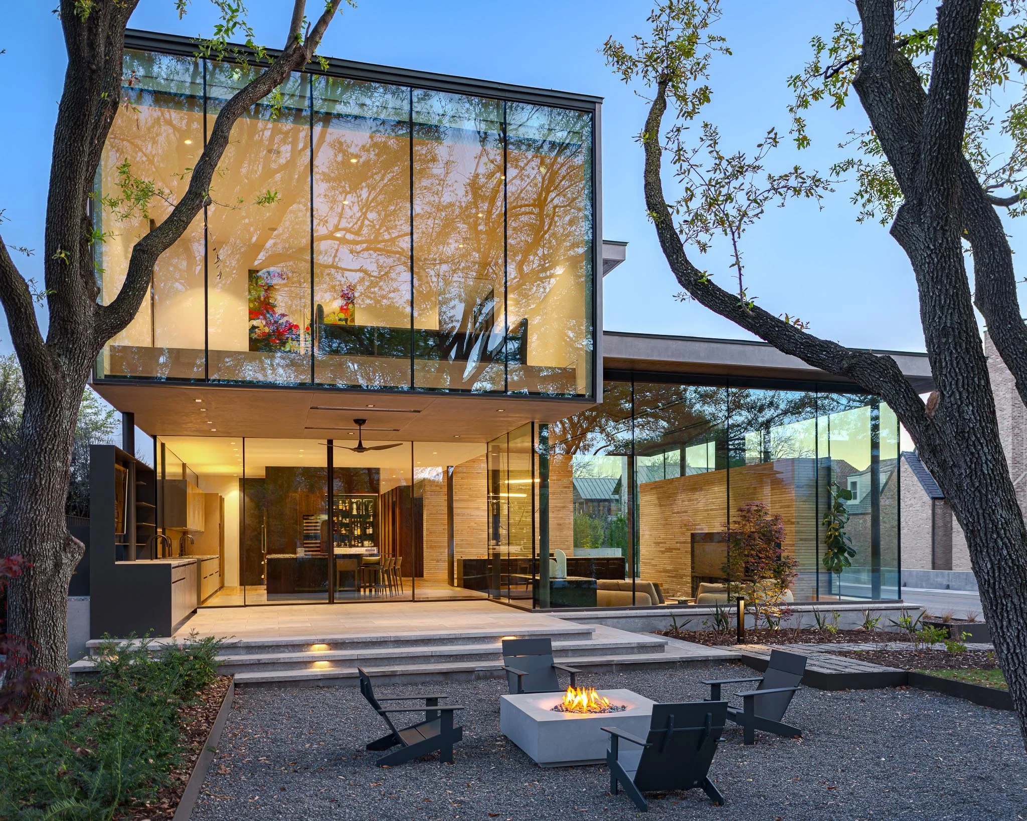 Modern luxury residence exterior with expansive glass walls, courtyard fire feature, and seamless indoor-outdoor living. SmithArc Architects.