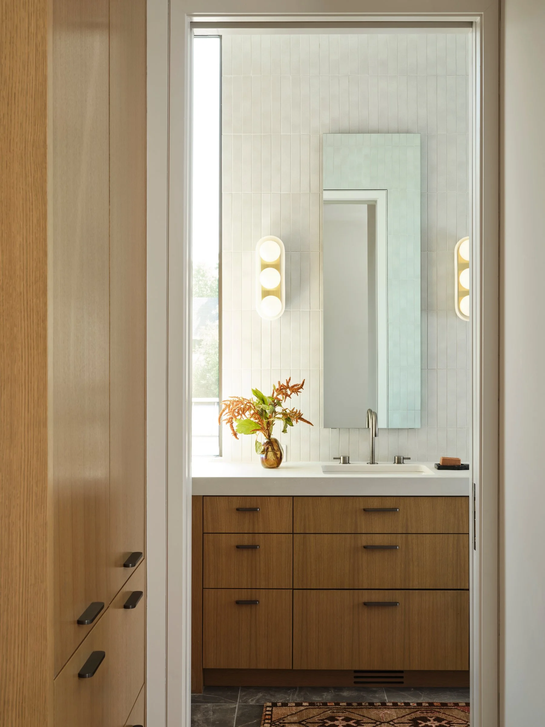 Minimal modern bathroom with custom wood vanity, white tile walls, and integrated lighting in a refined contemporary home.
