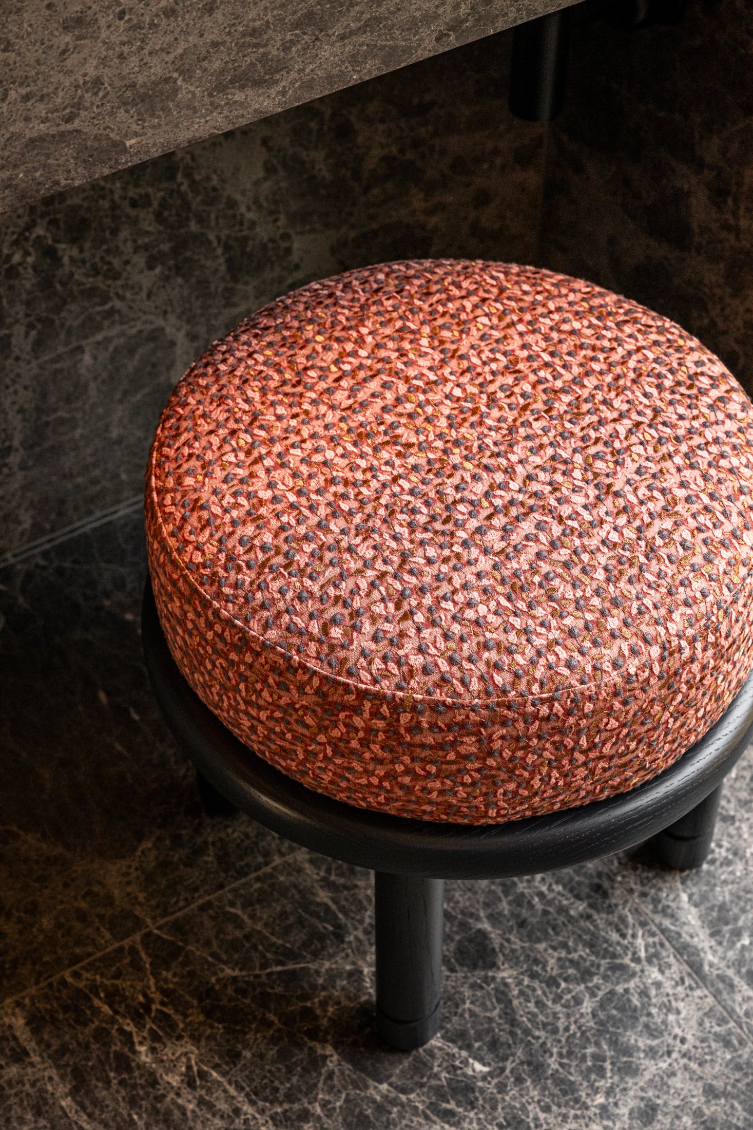 Upholstered stool with textured fabric against dark stone flooring, emphasizing contrast and tactile material layering in modern interior design.