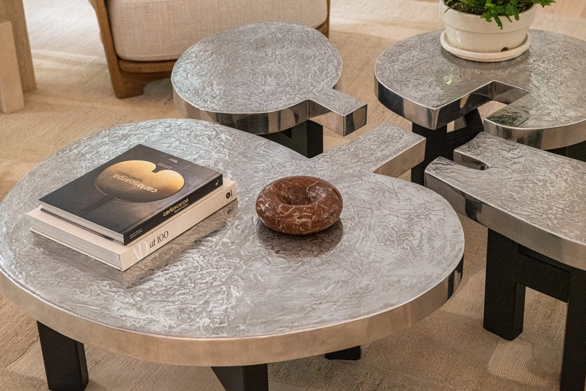 A cluster of sculptural cast metal Josephine tables by Ado Chale creates a functional centerpiece with strong material presence. Textural surfaces and precise forms add depth while maintaining the room’s quiet architectural language.