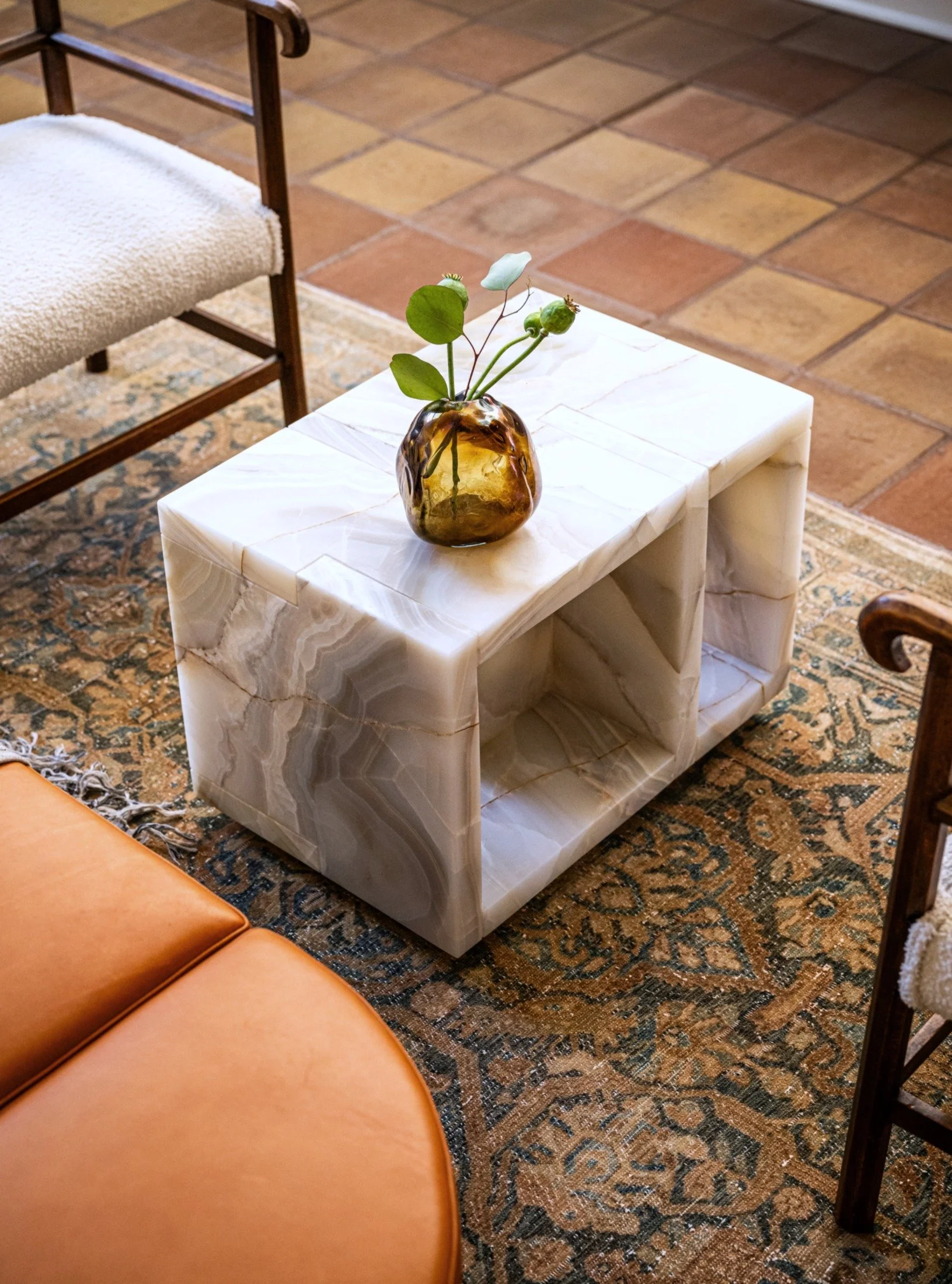 Solid white onyx stone side table with sculptural form and natural veining, designed by joshua rice styled with glass vessel and greenery in a curated modern interior.