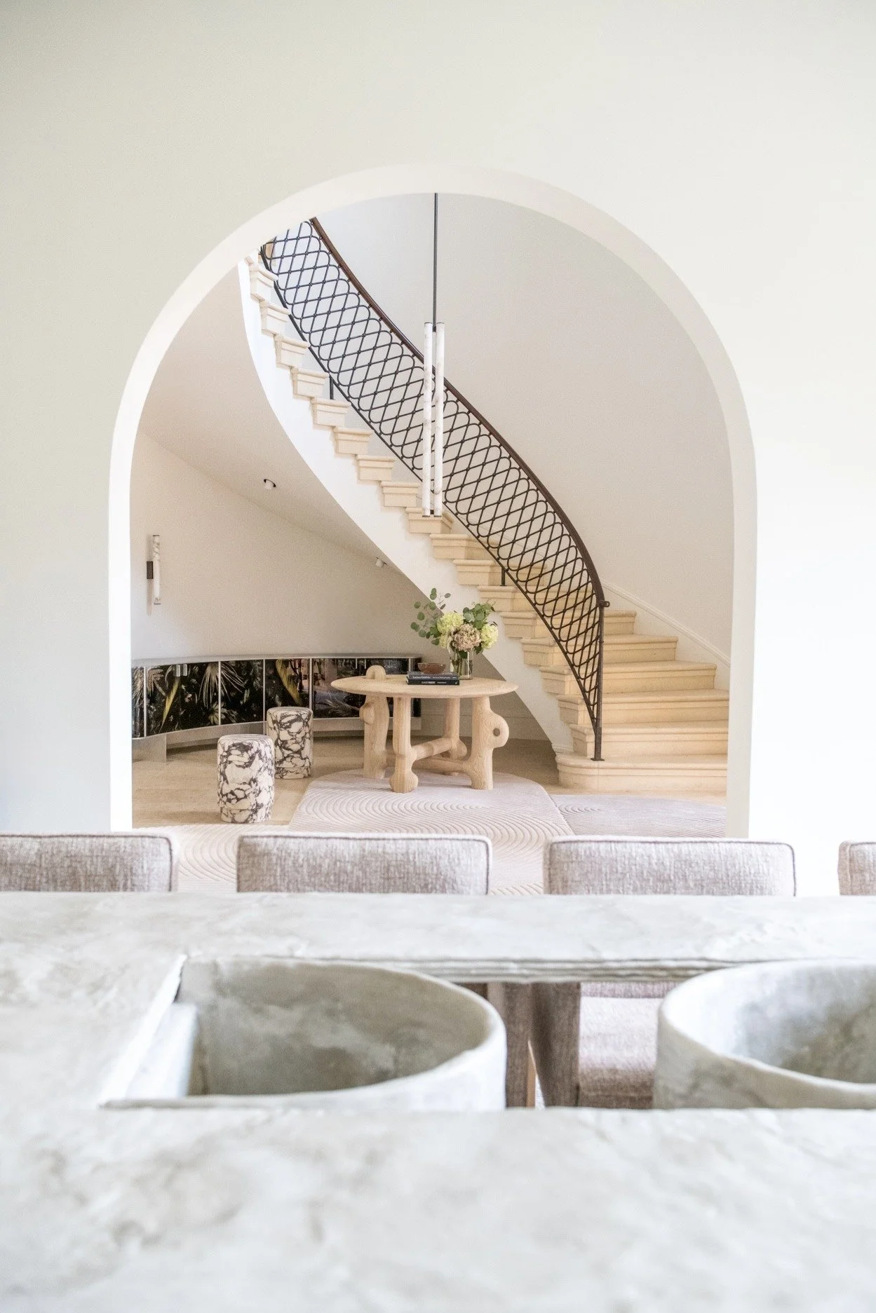 Arched foyer with sweeping staircase, custom iron railing, and sculptural stone furnishings creating a quiet, elegant modern residential entry.  Marcin Rusak custom cabinet and a table by Casey McCafferty. 