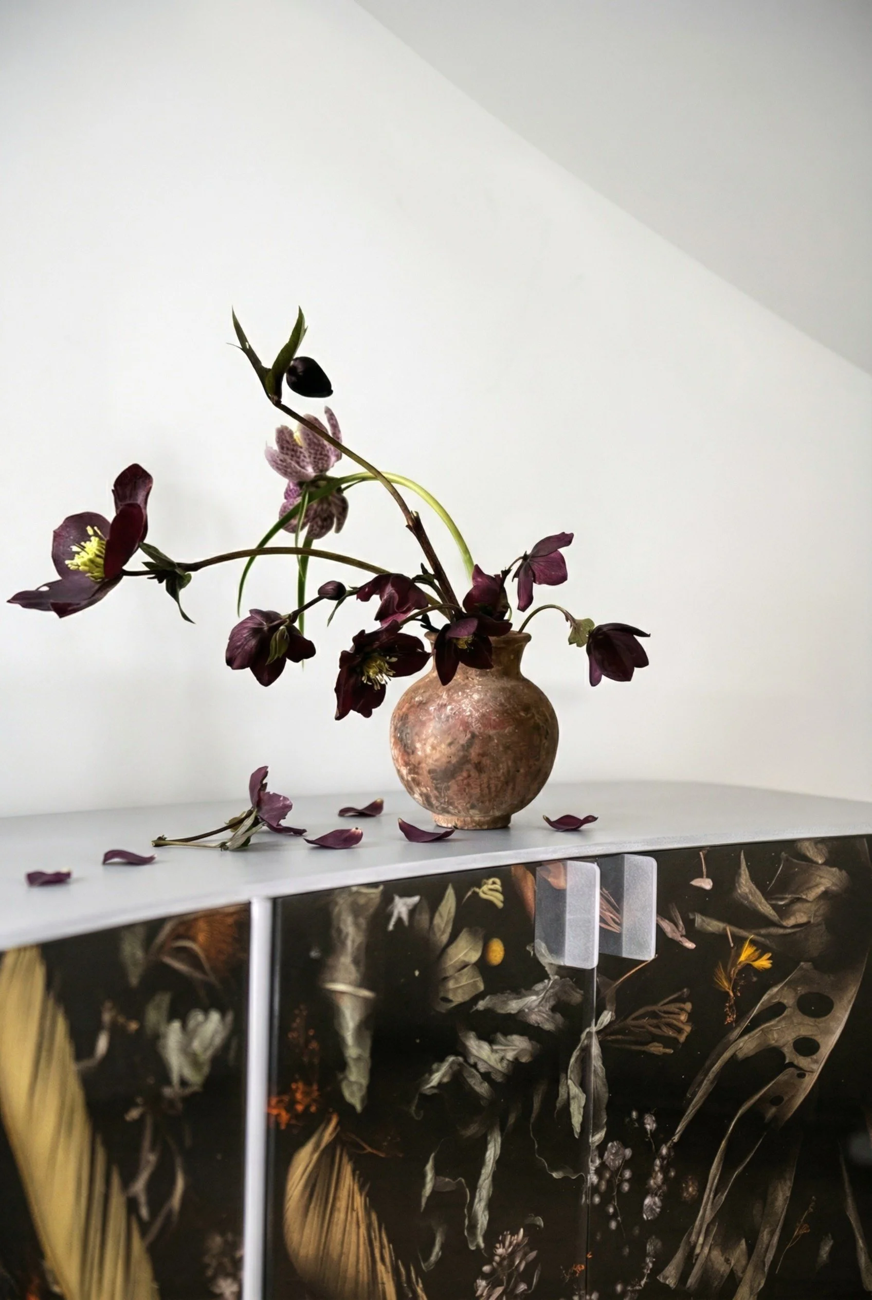 A decorative vignette featuring sculptural florals and a botanical custom Flora cabinet by Marcin Rusak introduces softness against clean architectural lines. Collected objects and subtle patina bring warmth to the composition.