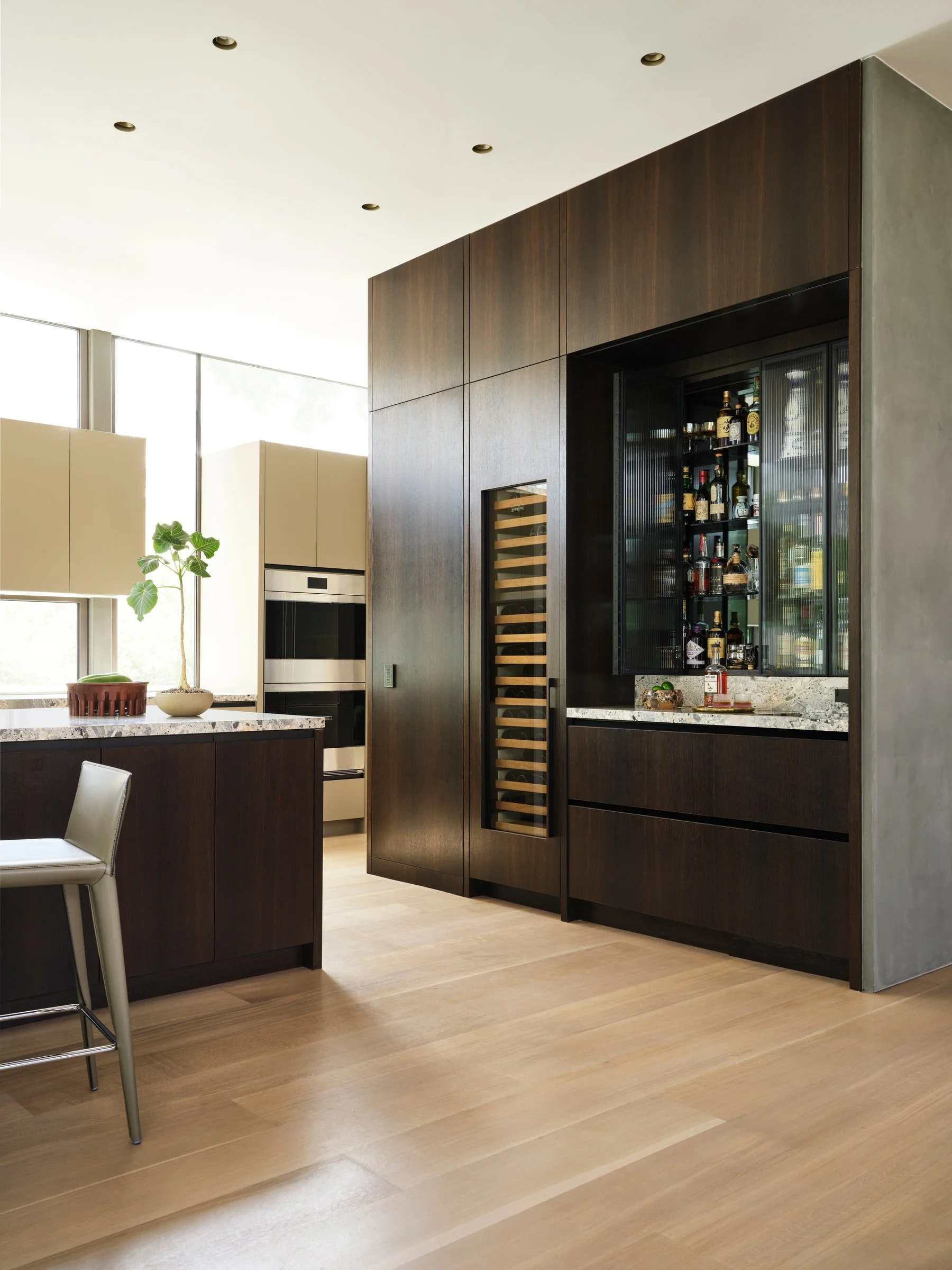 Modern kitchen with custom wood cabinetry, integrated wine storage, and stone countertops, emphasizing clean lines and material warmth.