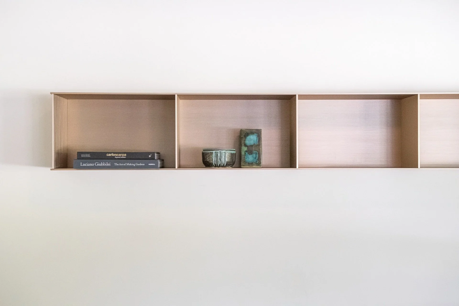 Detail of custom floating anodized aluminum shelf by Jonathan Nesci styled with collectible books, ceramics, and sculptural objects against a clean architectural white wall.