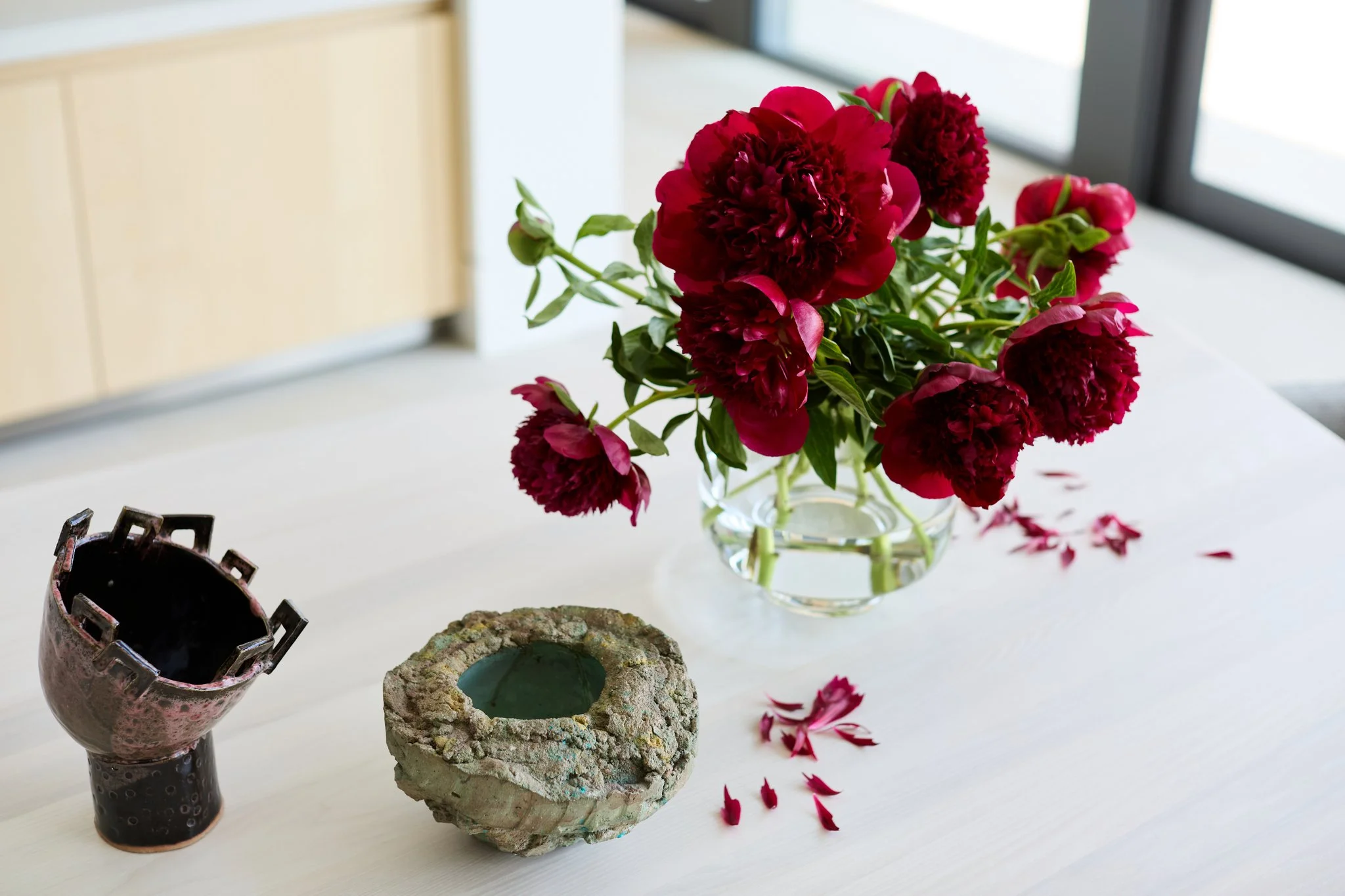 Red peony floral arrangement in glass vase on modern dining table with sculptural decorative vessel