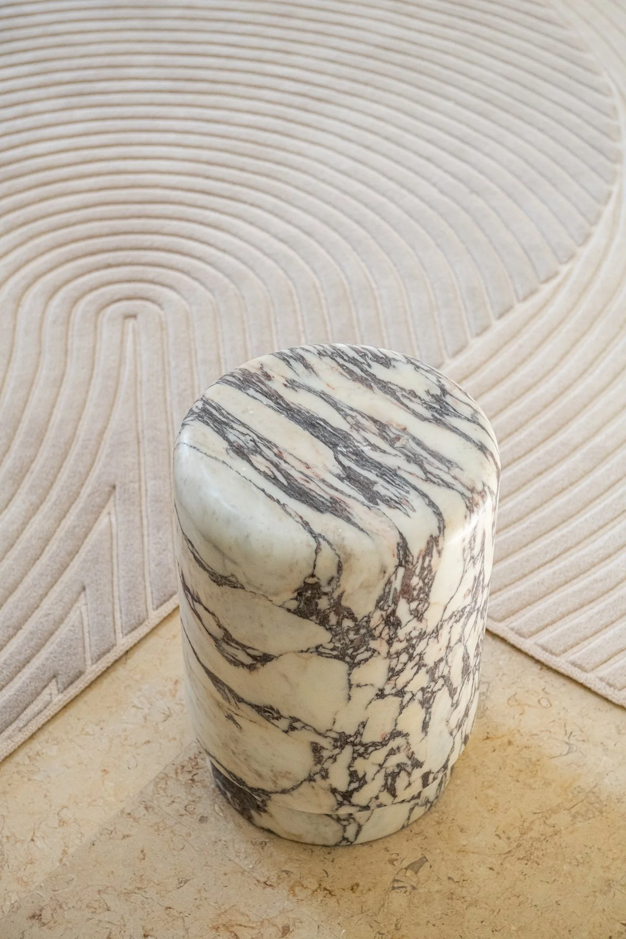 Marble accent stool by Michael Verheyden with dramatic natural veining placed against a sculptural patterned rug in a refined entry sequence.