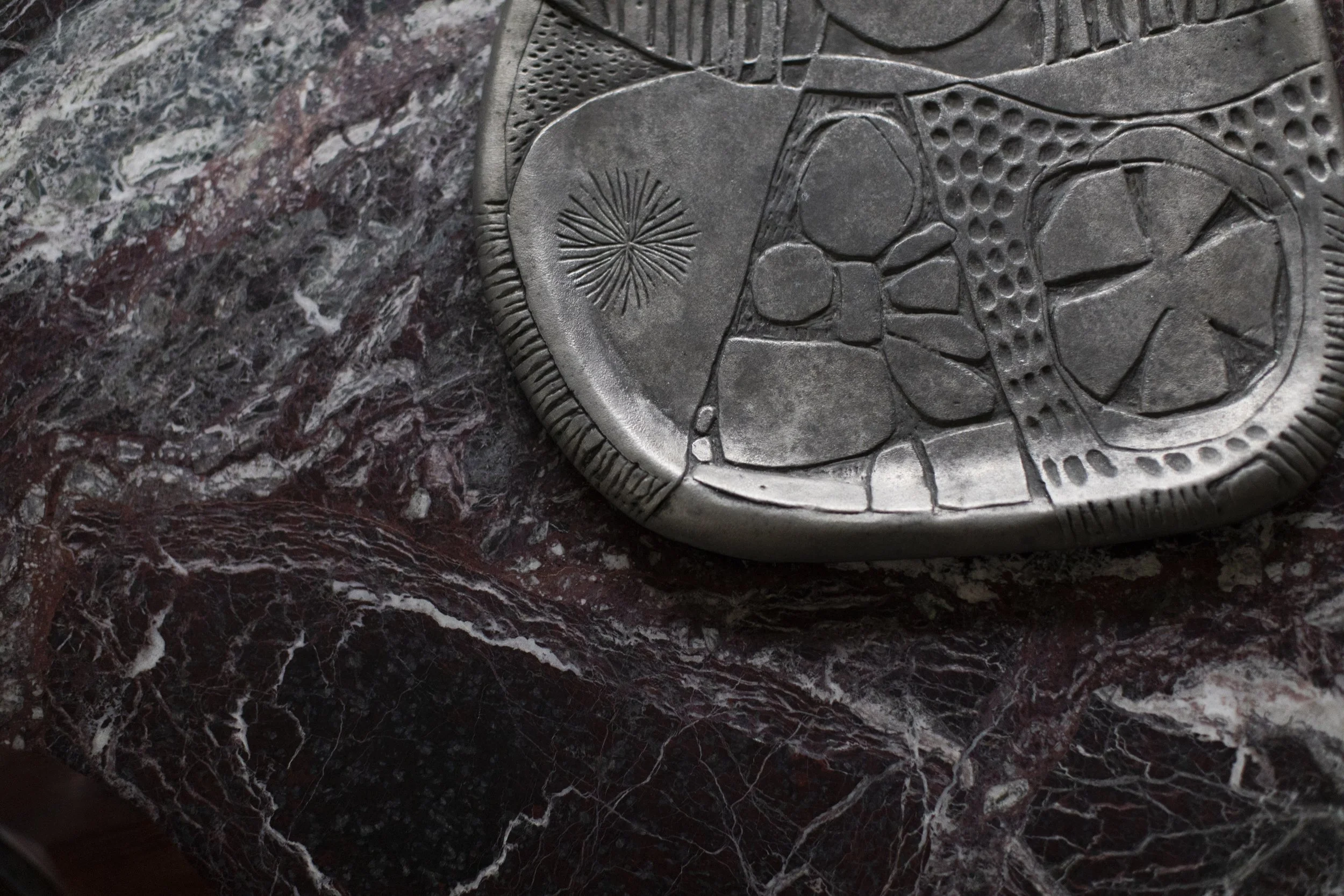 Textured metal tray or plate resting on richly veined burgundy marble surface donald drumm