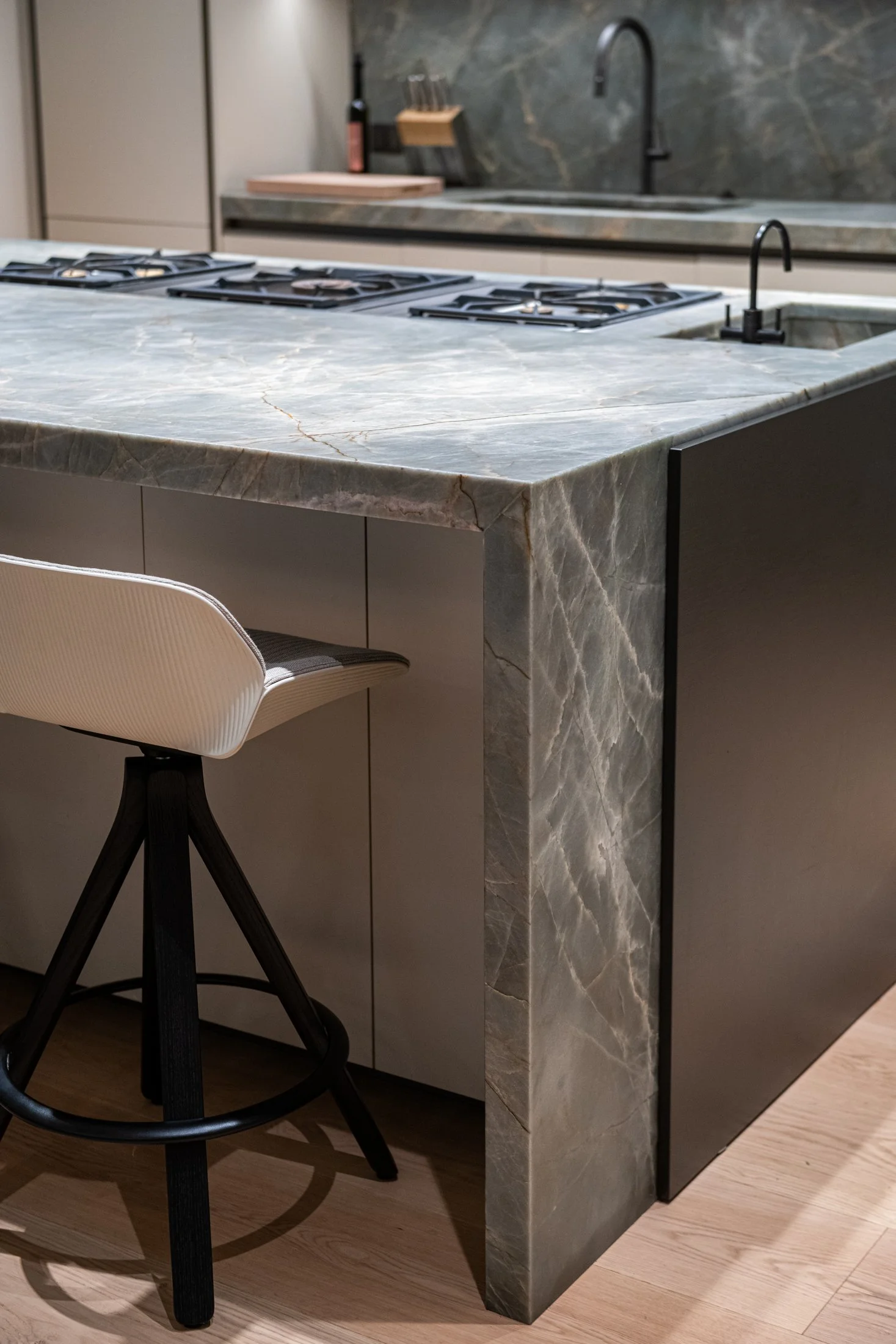 Thick-cut stone wraps the kitchen island in a seamless waterfall edge, highlighting natural veining and sculptural mass. Minimal cabinetry and matte finishes keep the focus on proportion and material integrity.