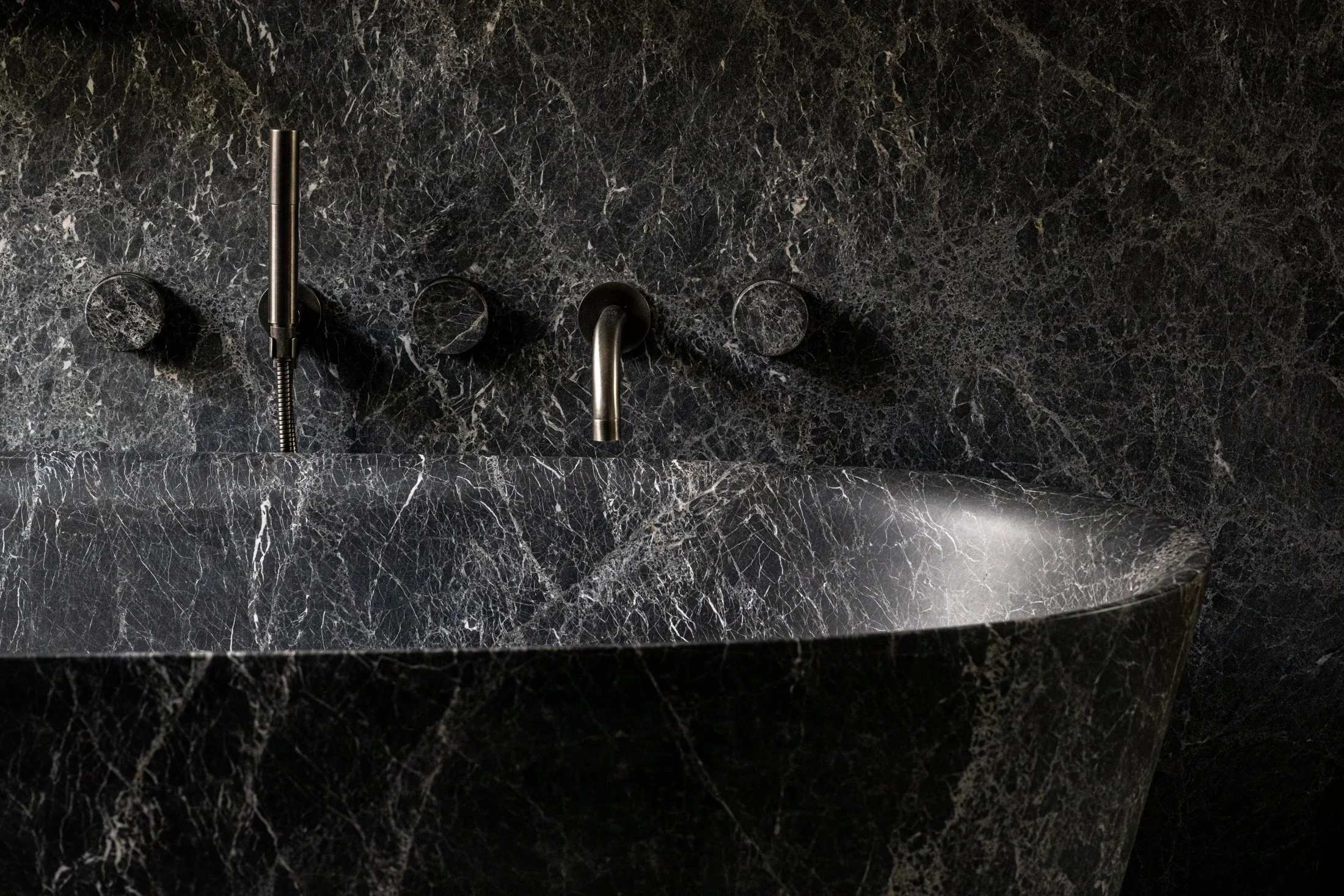 Detail of carved marble tub and integrated wall-mounted fixtures, emphasizing stone veining and precise hardware alignment.