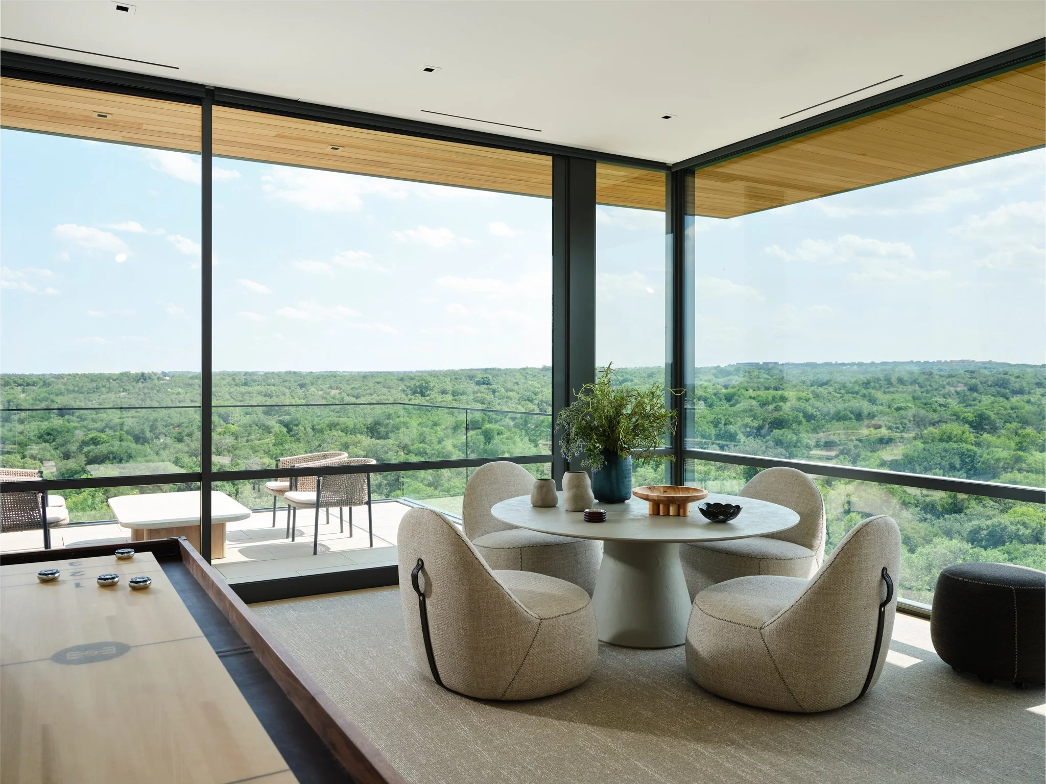Casual lounge and game area with sculptural lounge chairs and round table positioned beside expansive glass overlooking the Texas Hill Country.