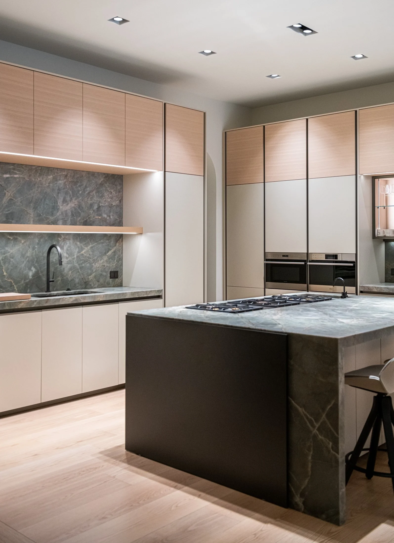 A tailored kitchen defined by a monolithic marble island, integrated cooktop, and warm oak cabinetry. Quiet architectural detailing and restrained materials create a refined, modern space with strong material presence.