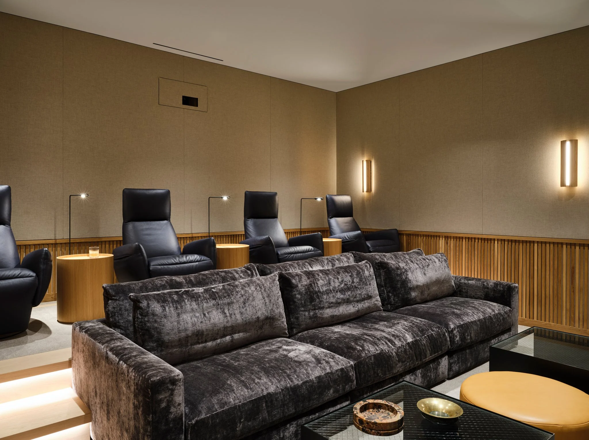 Private residential cinema with leather reclining chairs, velvet sofa, oak paneling, and integrated lighting. A refined home theater designed for comfort and architectural restraint.