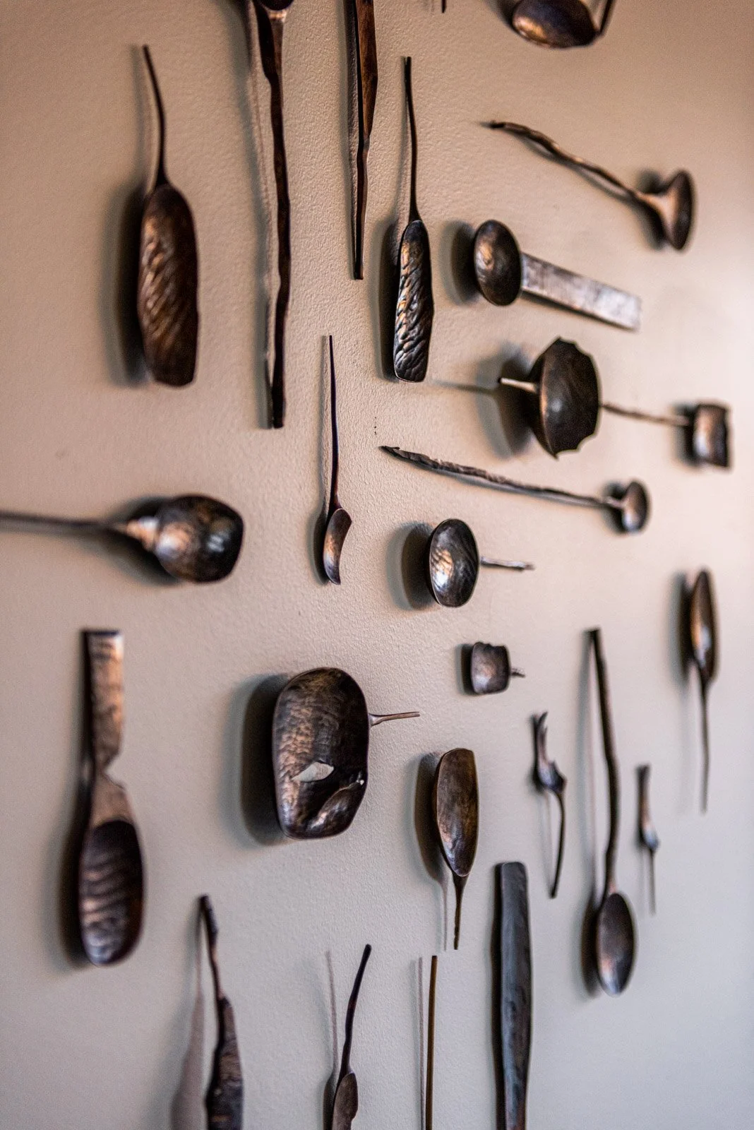 Hand carved wood wall sculpture composed of hammered spoon and tool forms arranged as contemporary art installation By Marie Eklund