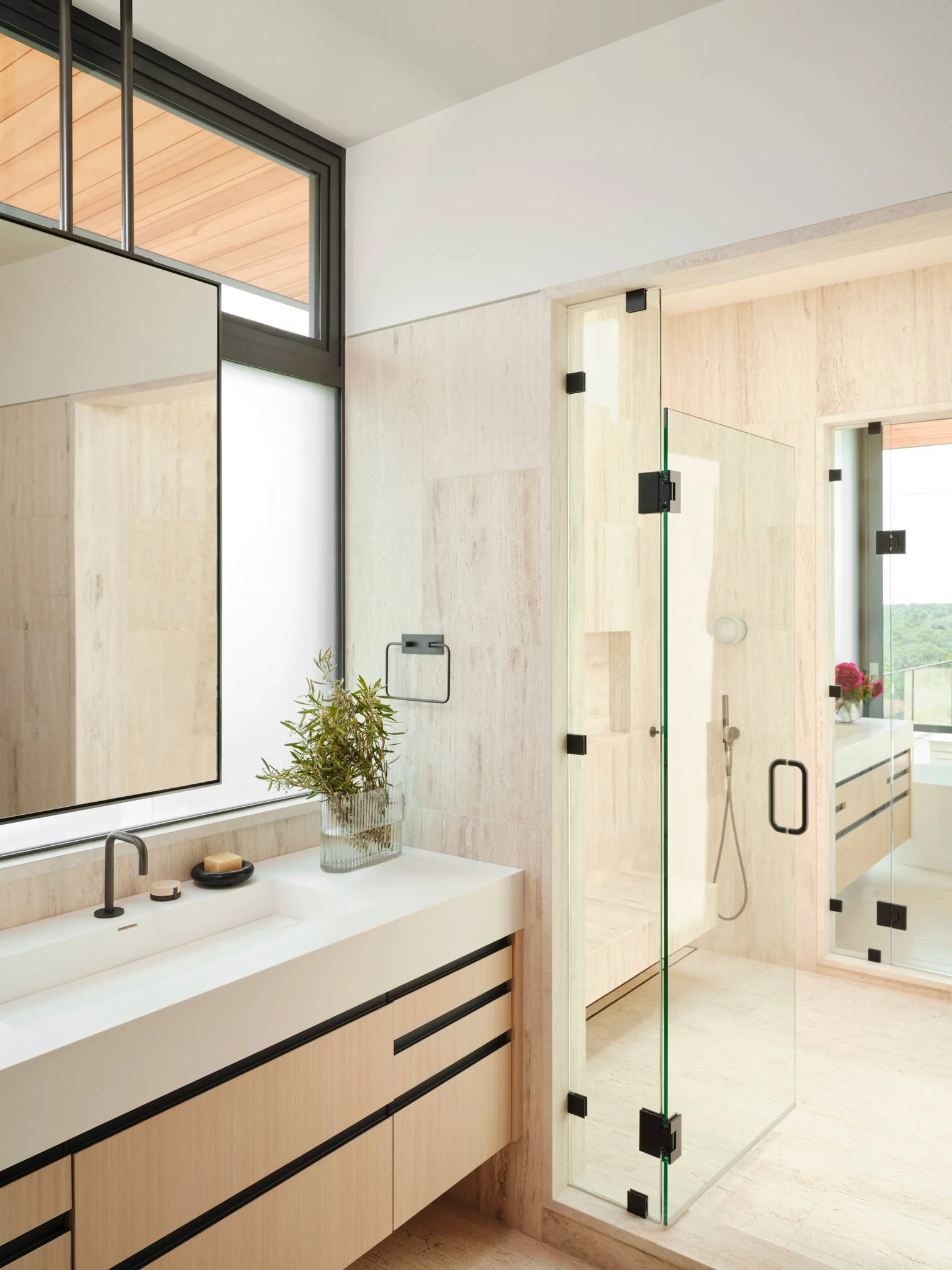 Minimal bathroom featuring floating oak vanity, integrated sink, and travertine stone walls. Frameless glass shower and restrained detailing create a serene spa-like interior.