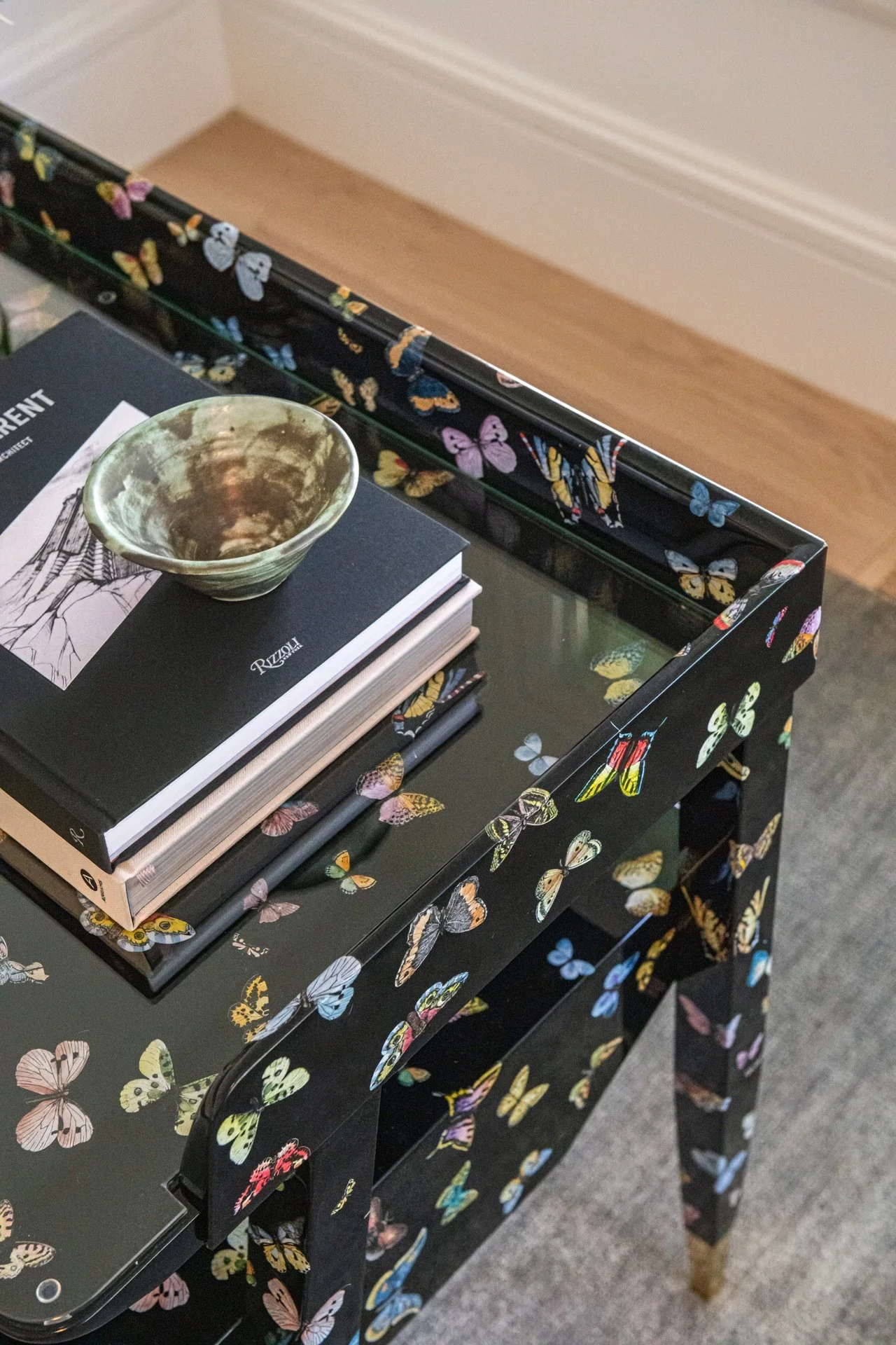 Lacquered butterfly motif console table with brass detailing by Gio Ponti and Piero Fornasetti, styled with art books and ceramic objects in a curated designer interior.